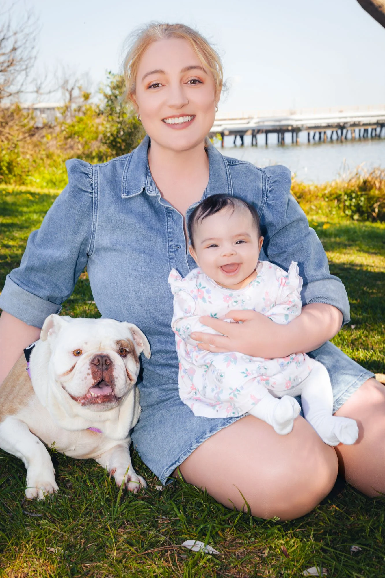 A mother sitting outdoors holding her baby with the family dog during a relaxed family photoshoot by Southern Exposure Photography.