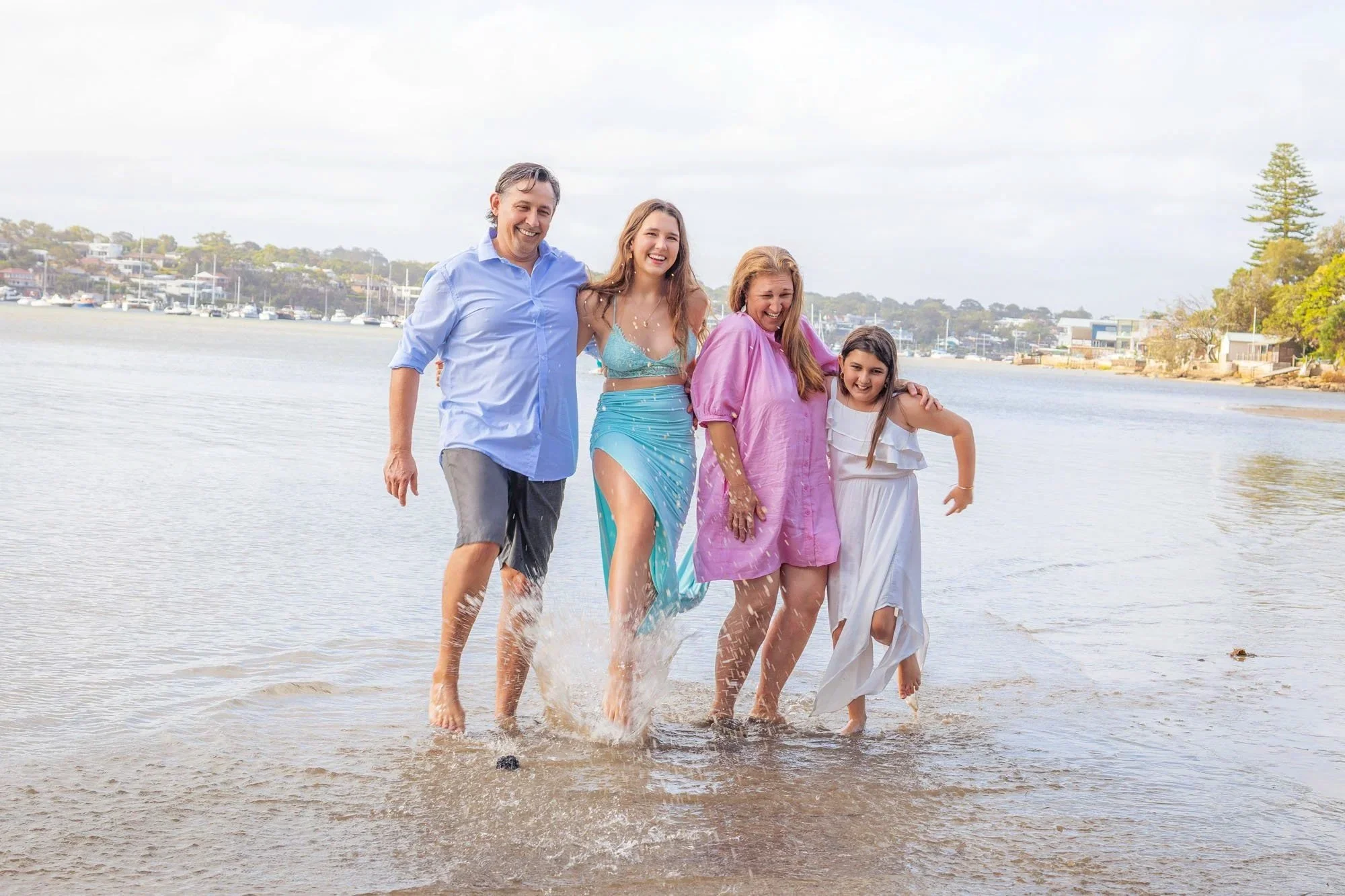A family of four laughing and walking through shallow water during a relaxed beach photoshoot in the Sutherland Shire by Southern Exposure Photography