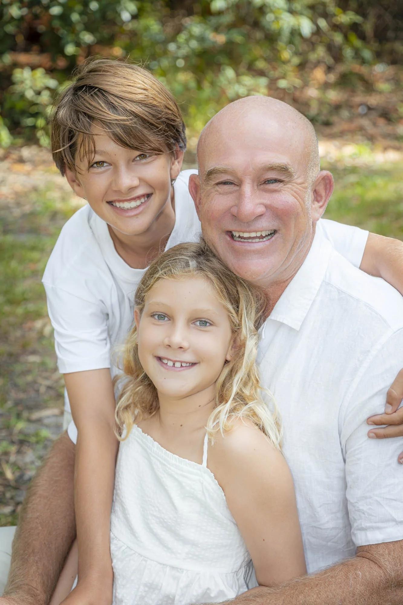 A happy family of three, a father and his two children, smiling outdoors during daytime.