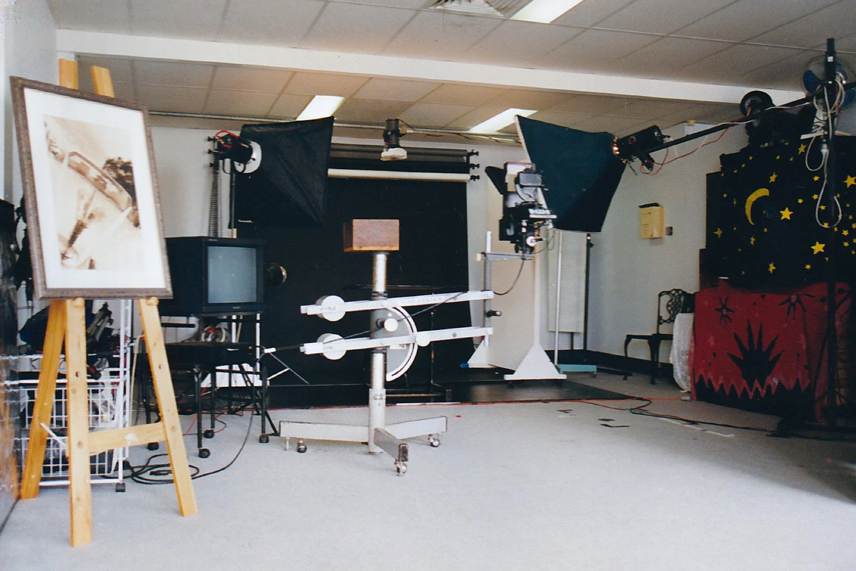 A photography studio with lighting equipment, a small TV, a camera on a tripod, and a backdrop with celestial design.
