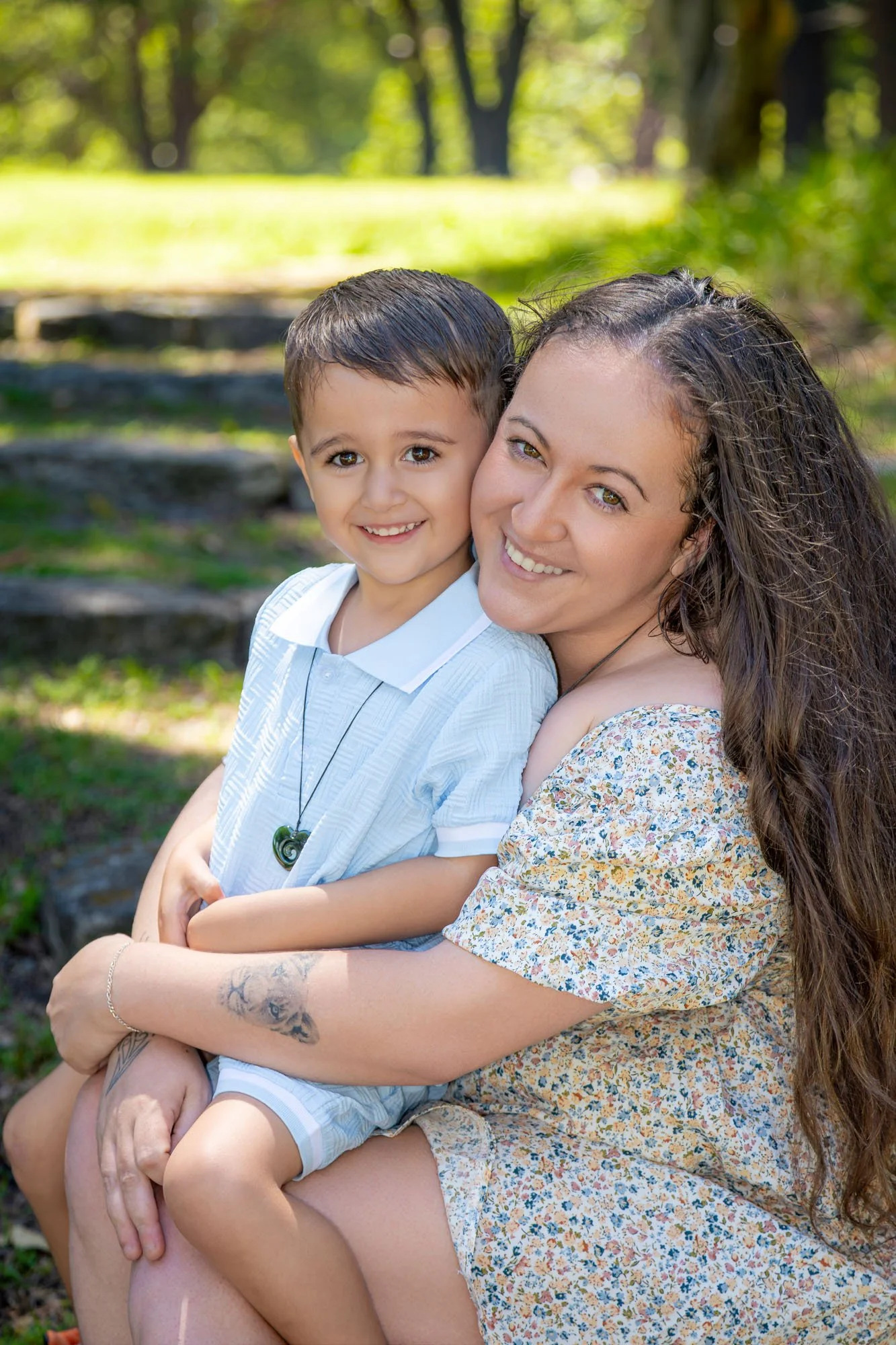 A mother and her young son smiling and embracing outdoors in a park with trees and sunlight during a relaxed outdoor family photoshoot by Southern Exposure Photography.