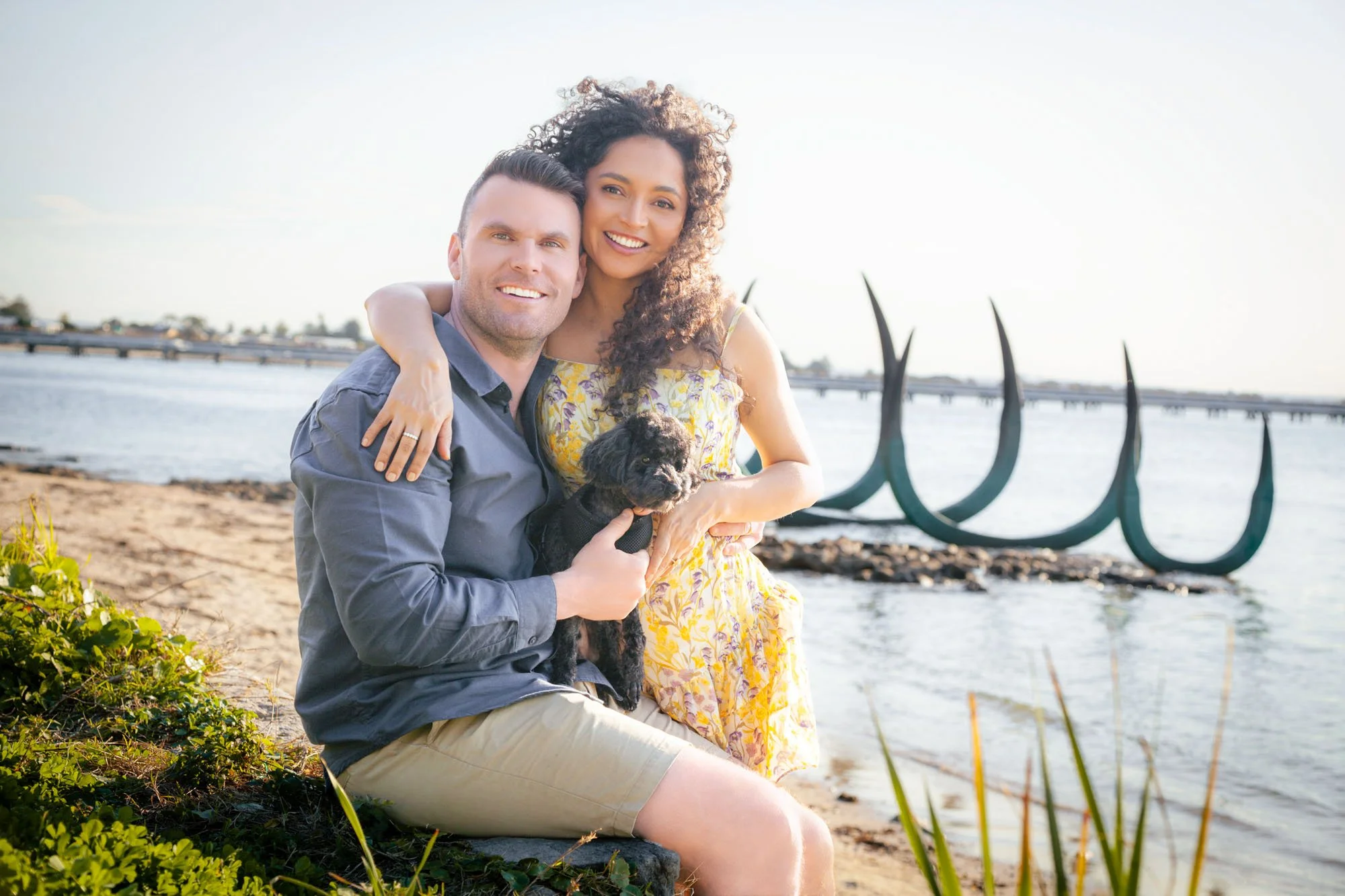 A couple sitting together by the water with their dog during a relaxed outdoor family photoshoot by Southern Exposure Photography.