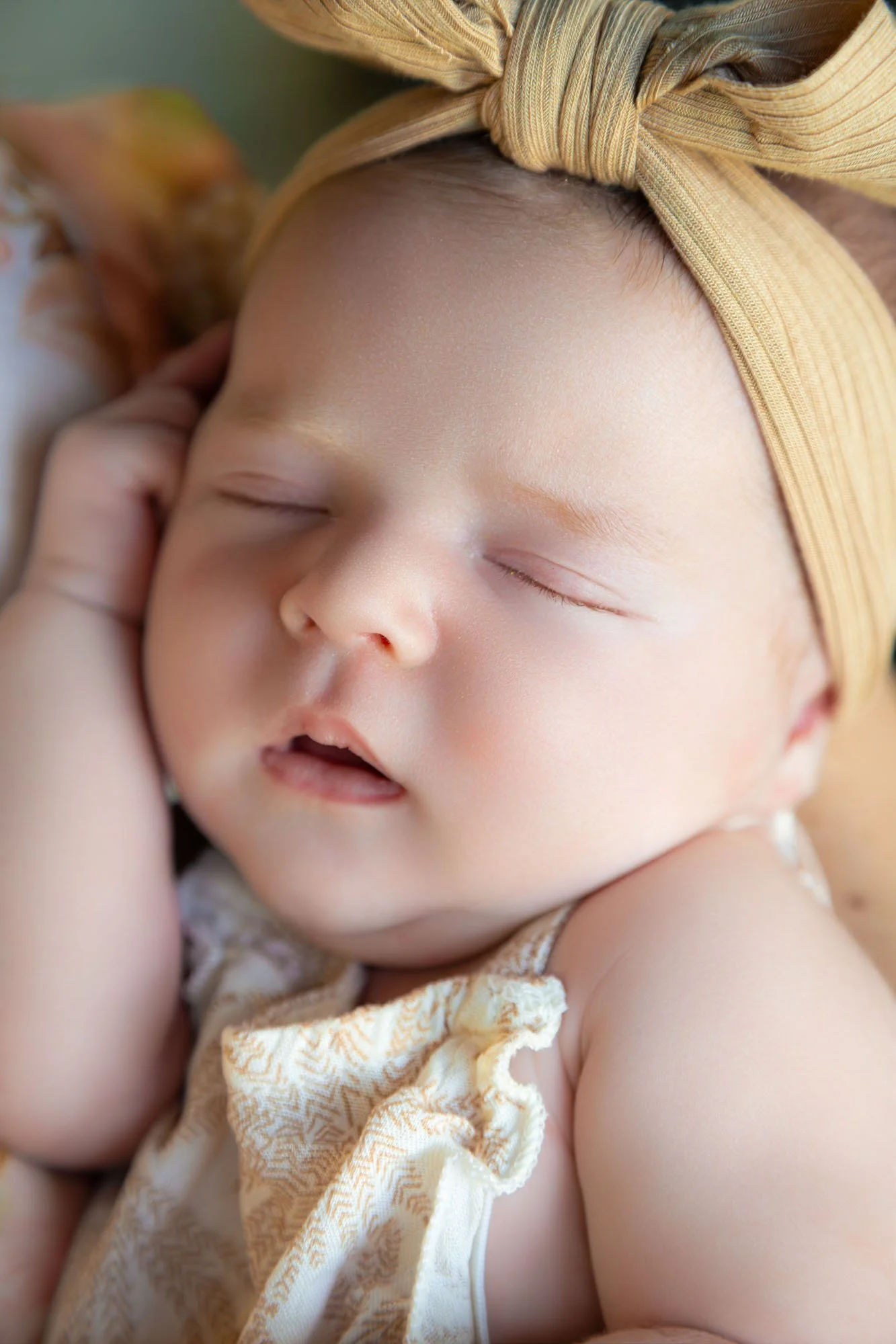A close-up of a sleeping baby's face with a hand resting near the cheek, wearing a tan headband and light-colored clothing during a relaxed family photoshoot by Southern Exposure Photography.