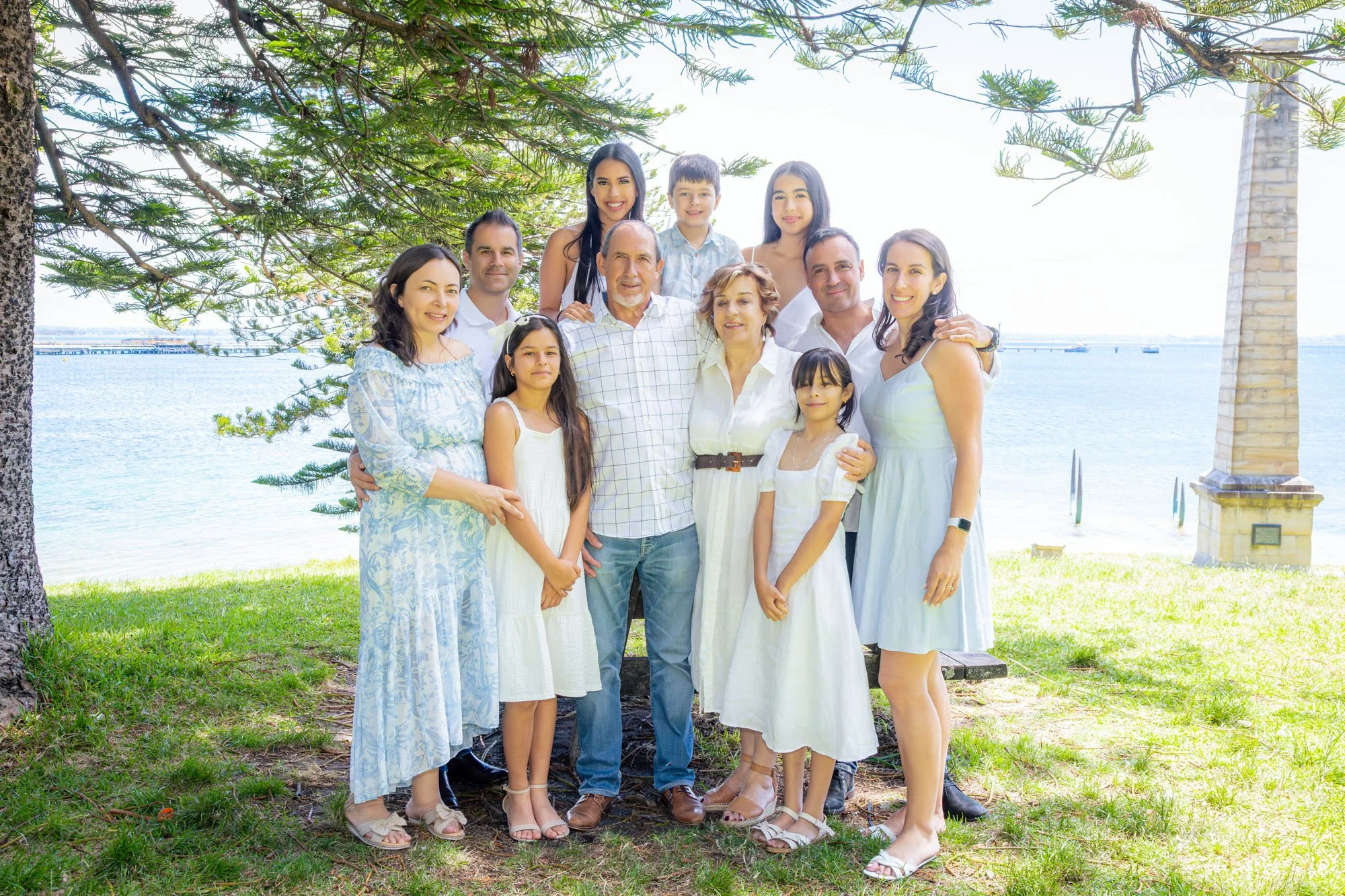 A large extended family standing together by the water during a relaxed outdoor family photoshoot by Southern Exposure Photography.
