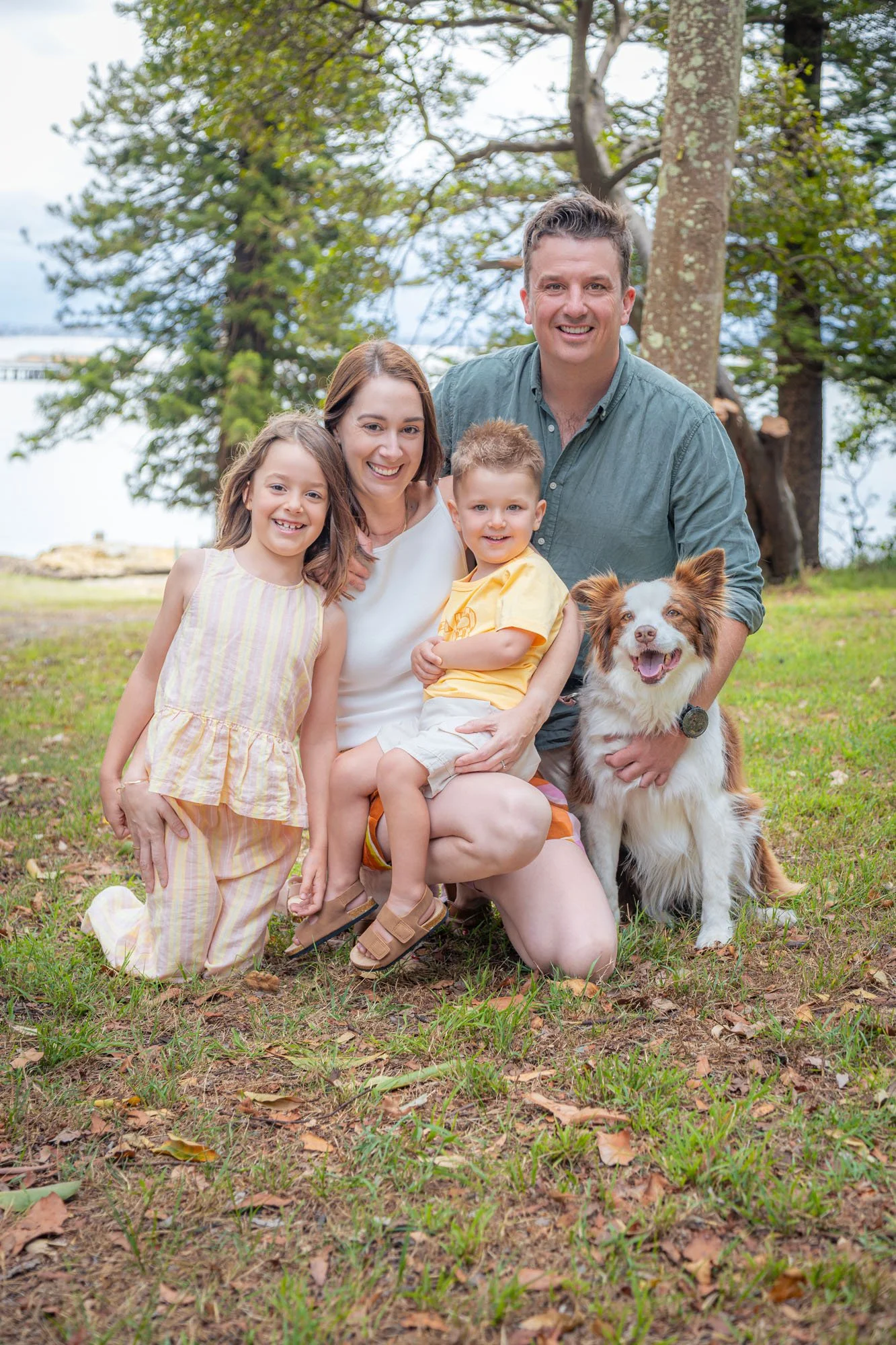 A happy family of four with a dog outdoors in a park during daytime, all smiling during a relaxed outdoor family photoshoot by Southern Exposure Photography.