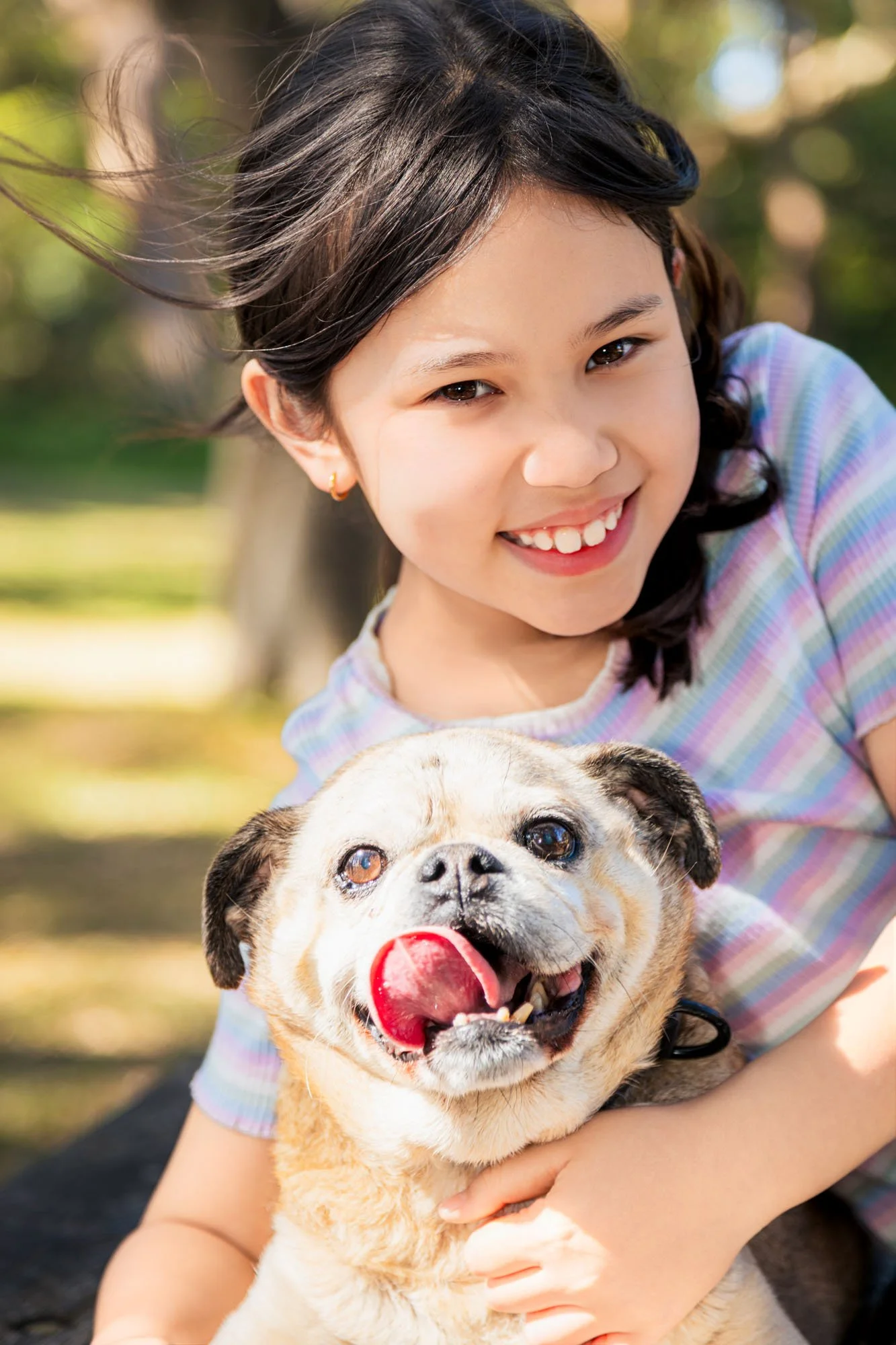 A young girl smiling while holding her dog during a relaxed outdoor family photoshoot by Southern Exposure Photography.