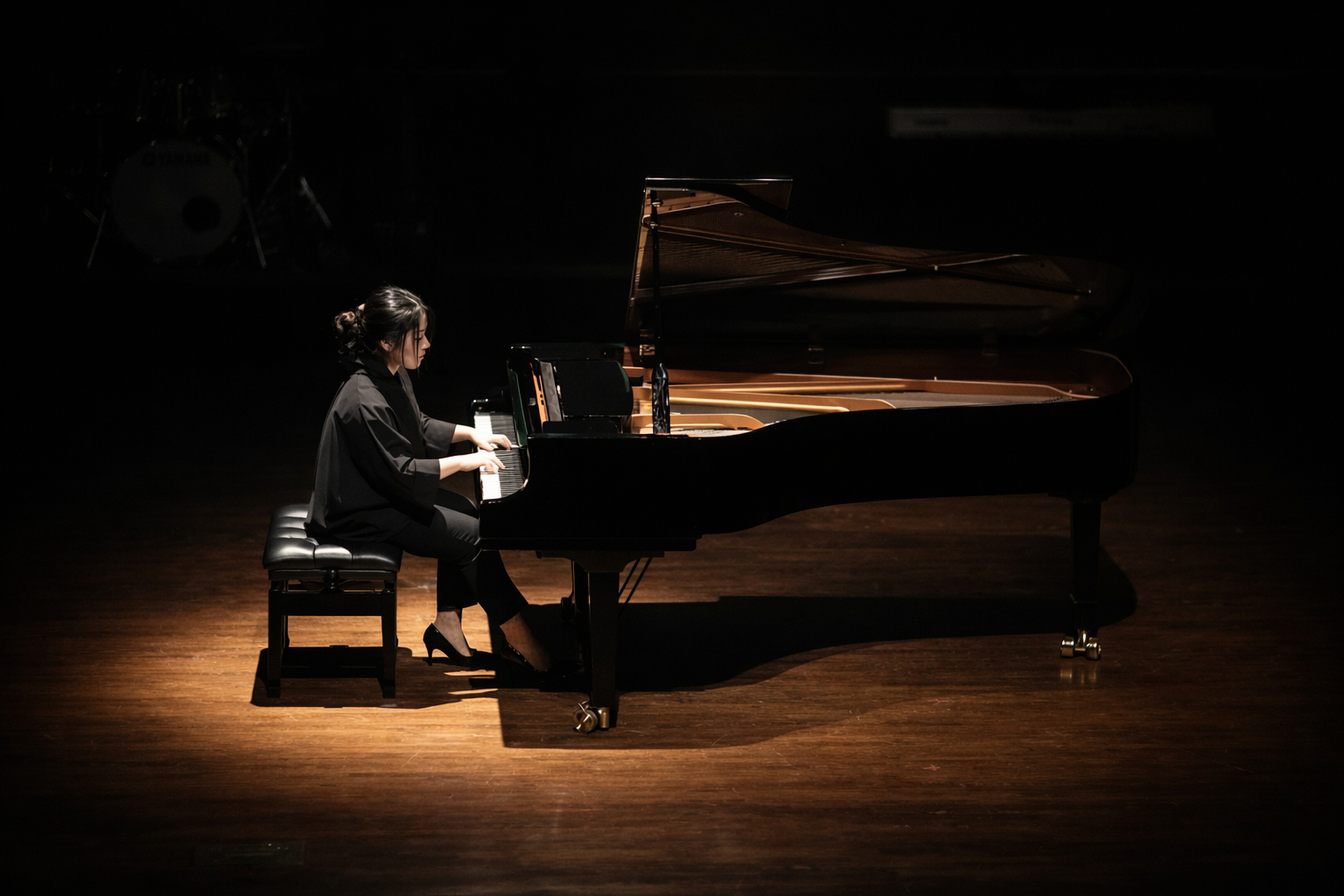 A woman playing a grand piano on a dark stage with a spotlight focused on her.