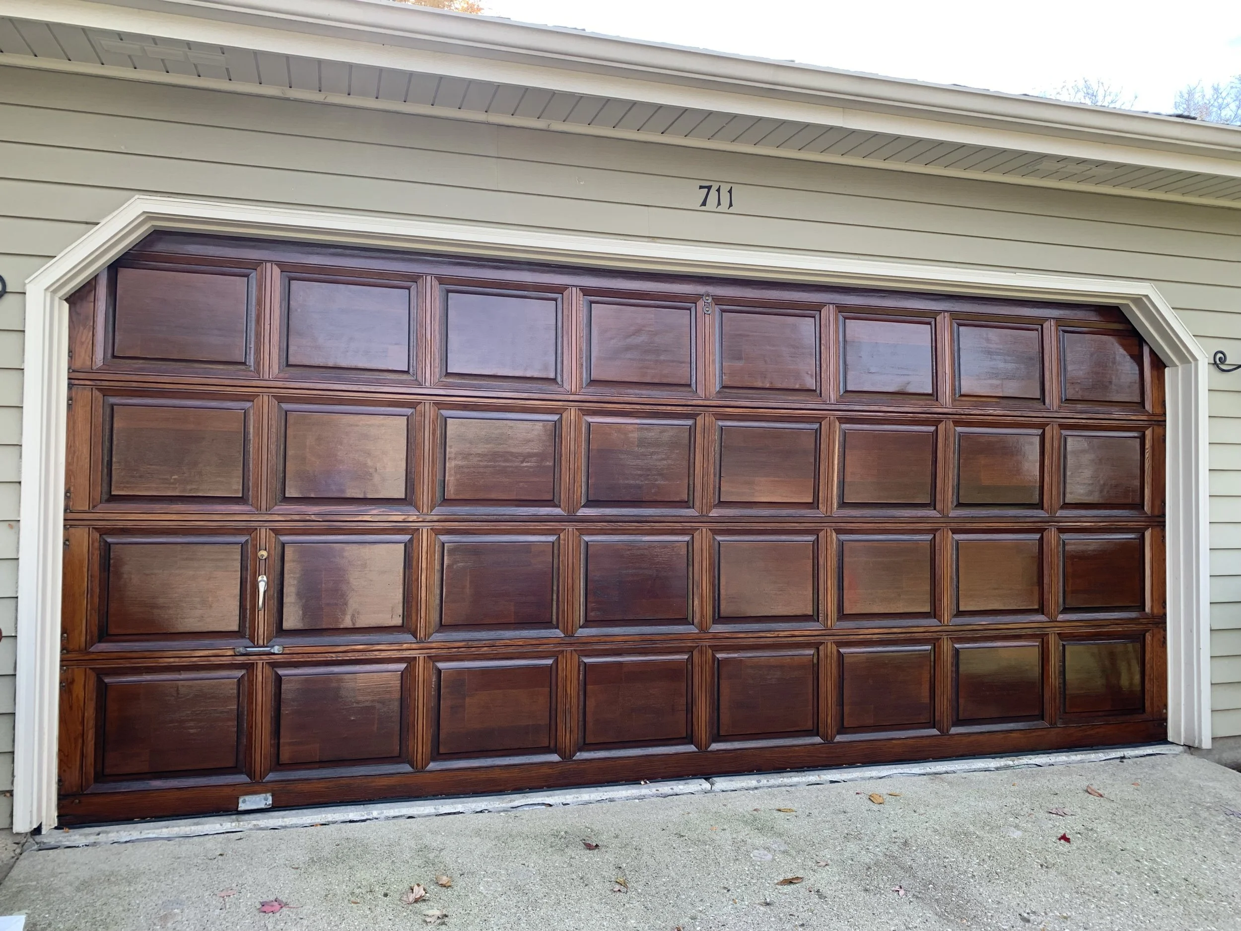 A wooden garage door with a rectangular panel design, located on a beige house with the number 711 above it.