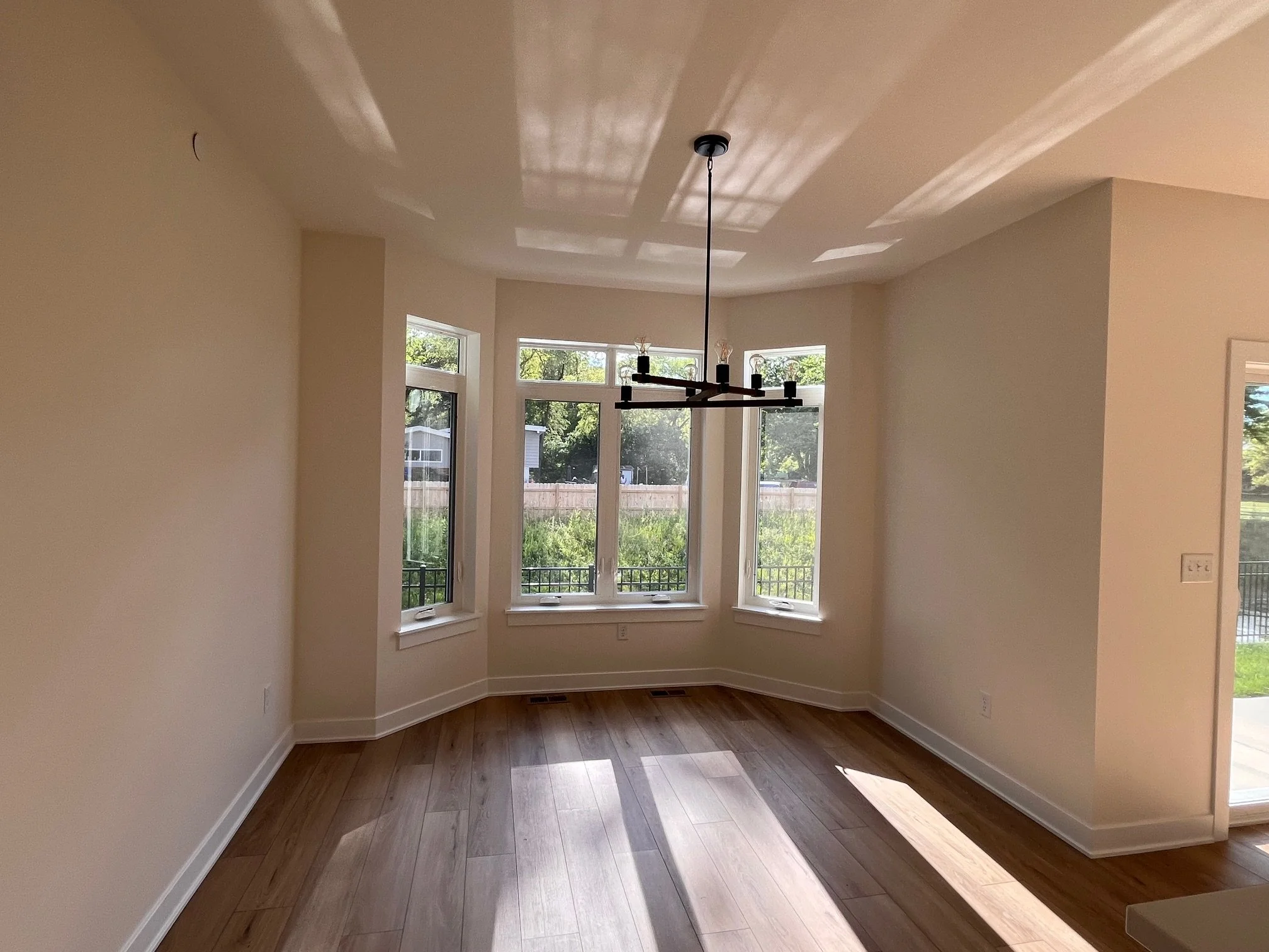 Empty room with large windows, hardwood floor, and a modern chandelier hanging from the ceiling.