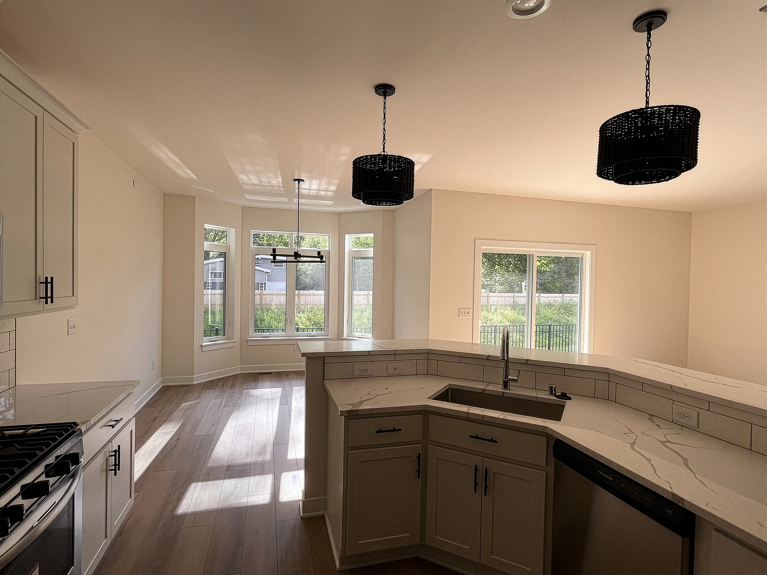 Kitchen and living area with large windows, white cabinets, marble countertops, black pendant lights, and light-colored wooden floors.