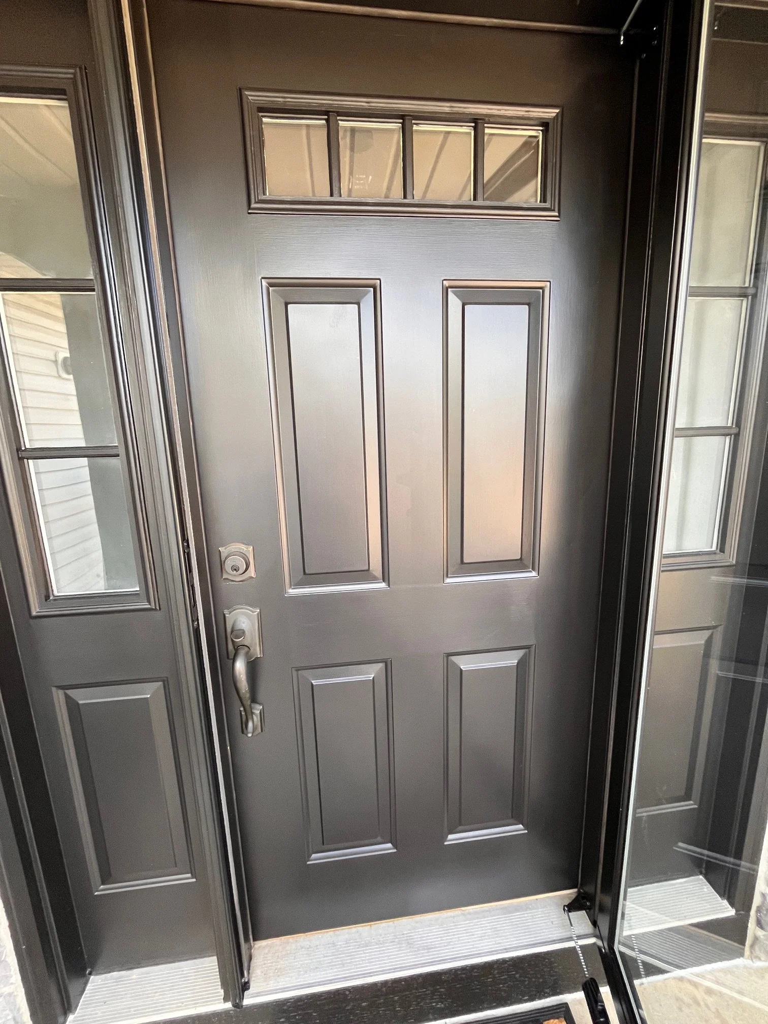 Front door with a small window at the top and glass sidelights on either side, with a handle and lock, leading into a house.