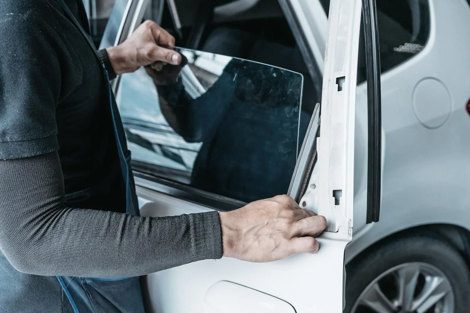 A person installing a window or glass panel into the side frame of a white vehicle.