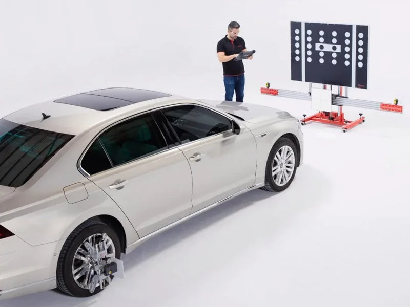 A man standing next to a silver sedan using a tablet, with a large projection mapping diagram of a car crash test ahead of him in a white studio.