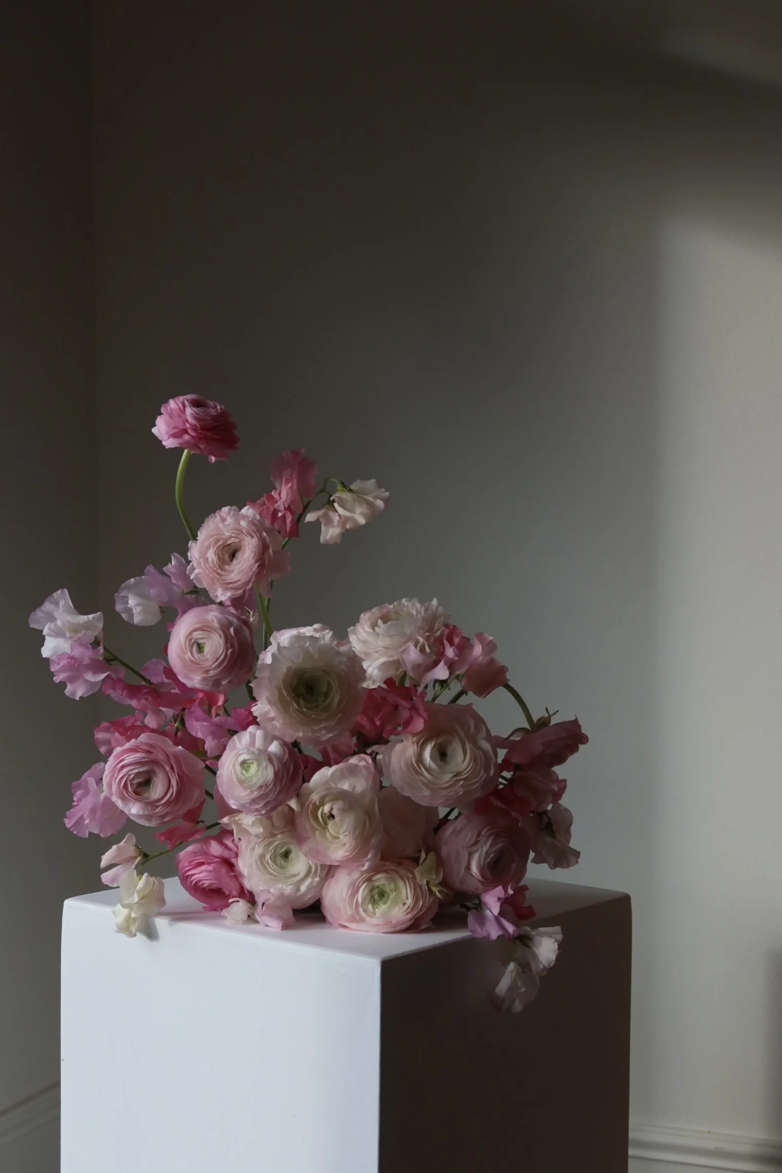 A bouquet of pink and white flowers arranged on a white pedestal against a neutral wall with soft lighting.