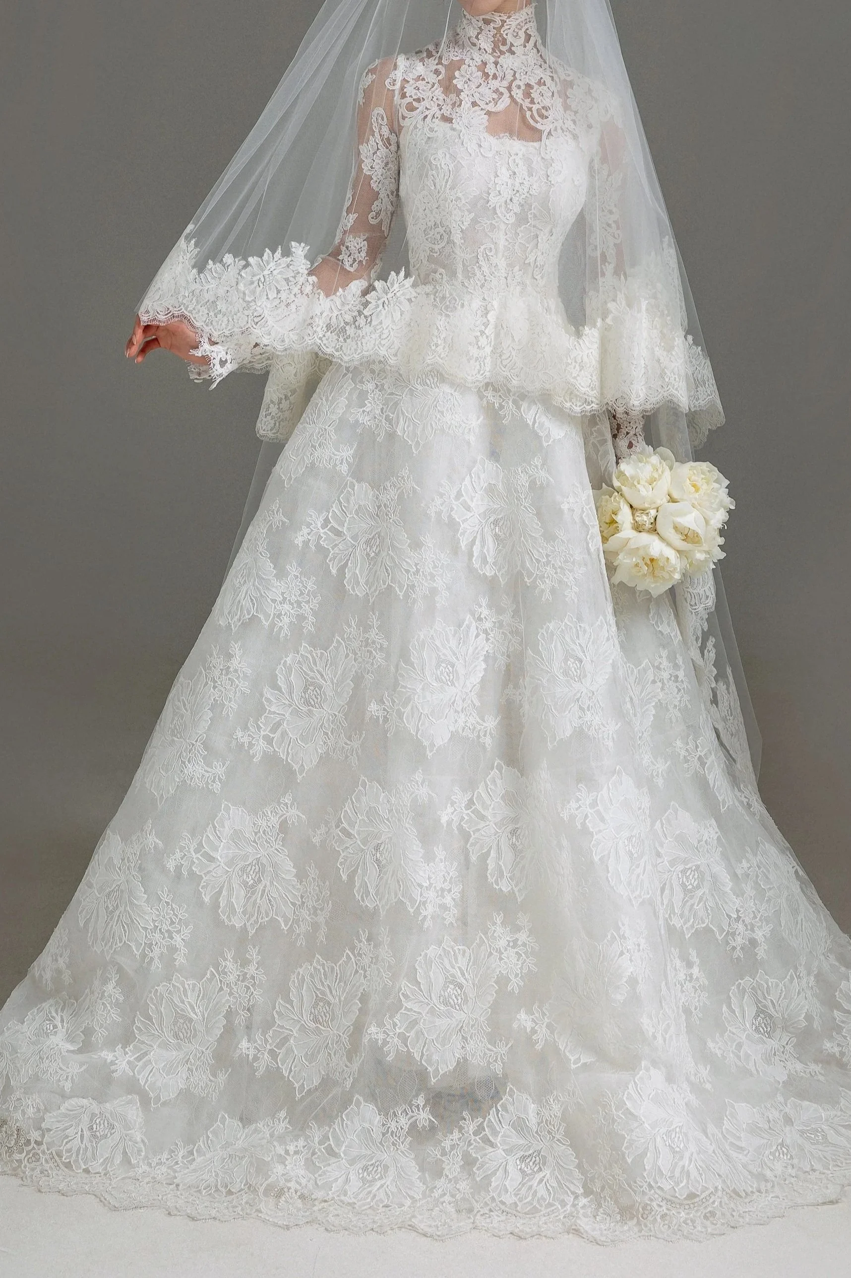 Wedding dress with lace details, a long veil, and a bouquet of white flowers.