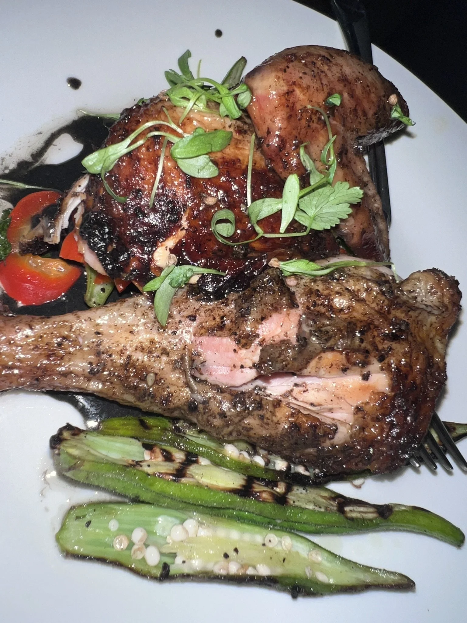 Grilled salmon with a glazed topping, garnished with microgreens, served with grilled green onions and cherry tomatoes on a white plate.