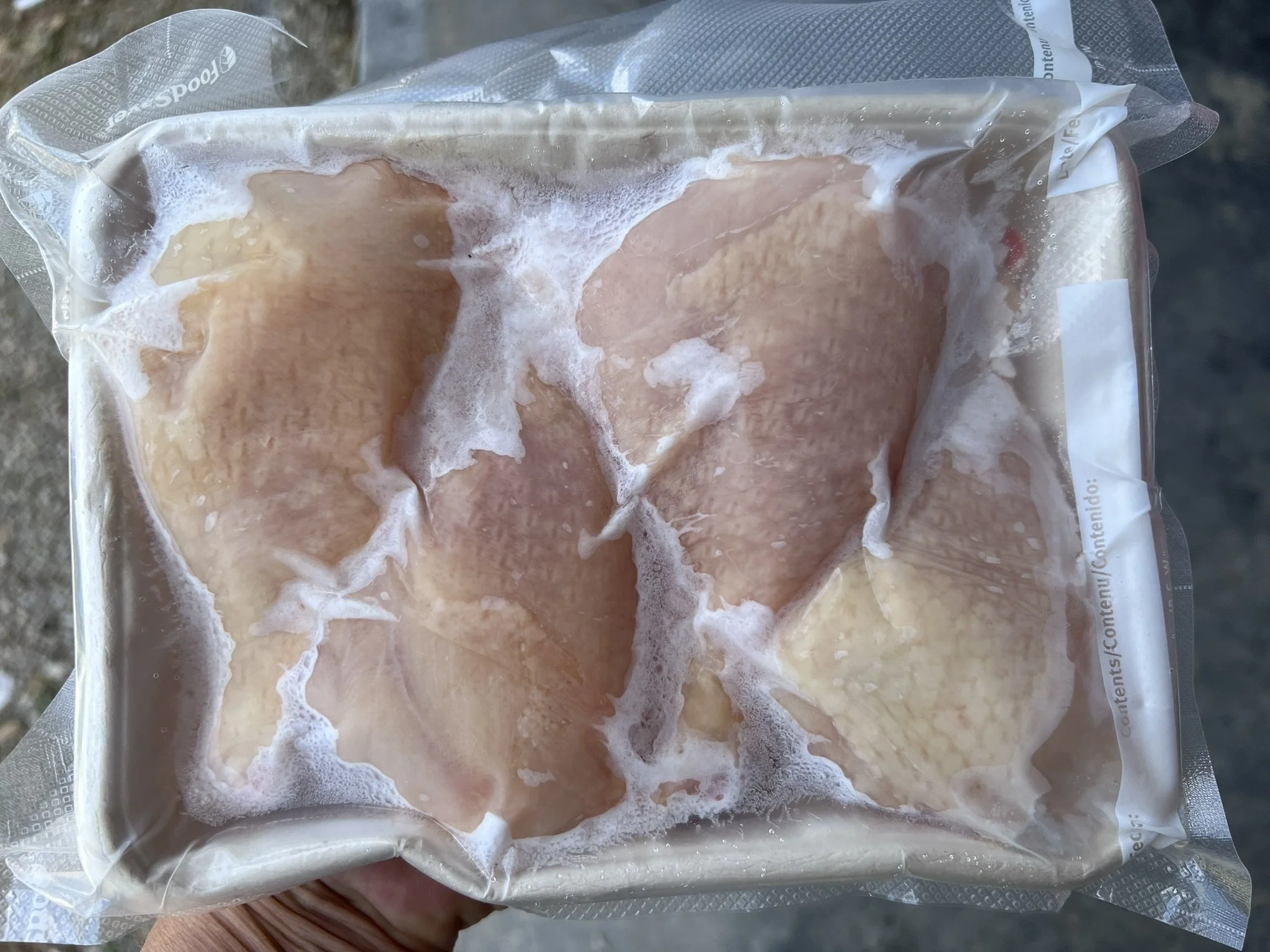 Frozen raw chicken breasts inside vacuum seal packaging.
