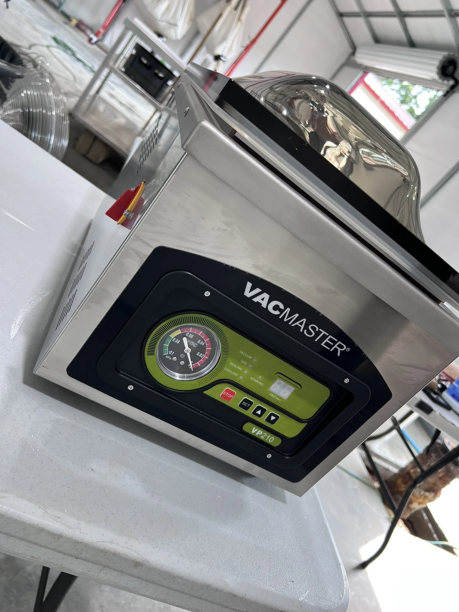 Close-up of a vacuum packaging machine with a digital control panel on a white surface, with a metal table and a blurred background of a workshop.