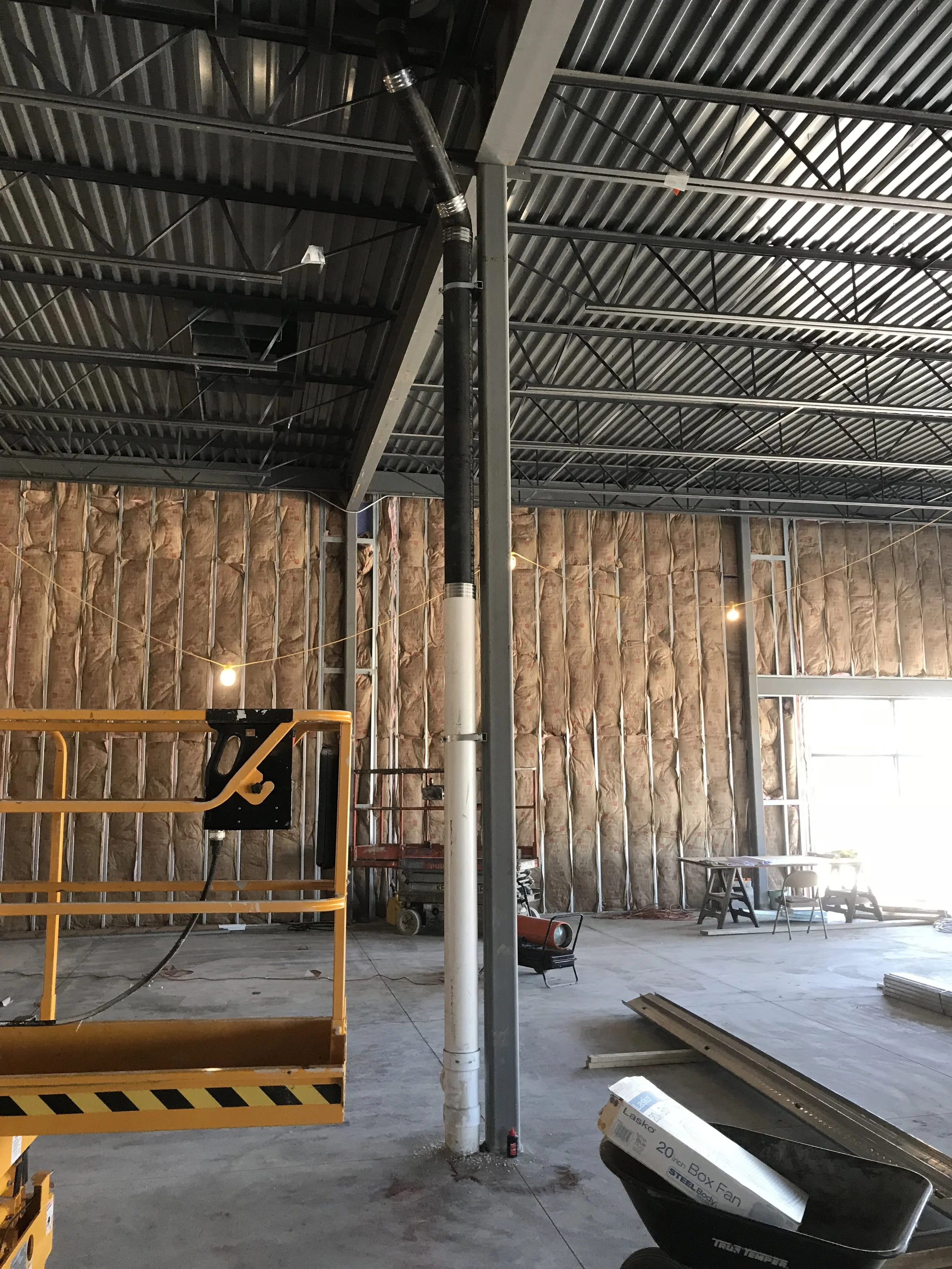 Construction site with insulated wall, metal ceiling, and various equipment including a cherry picker, stand, and boxes.