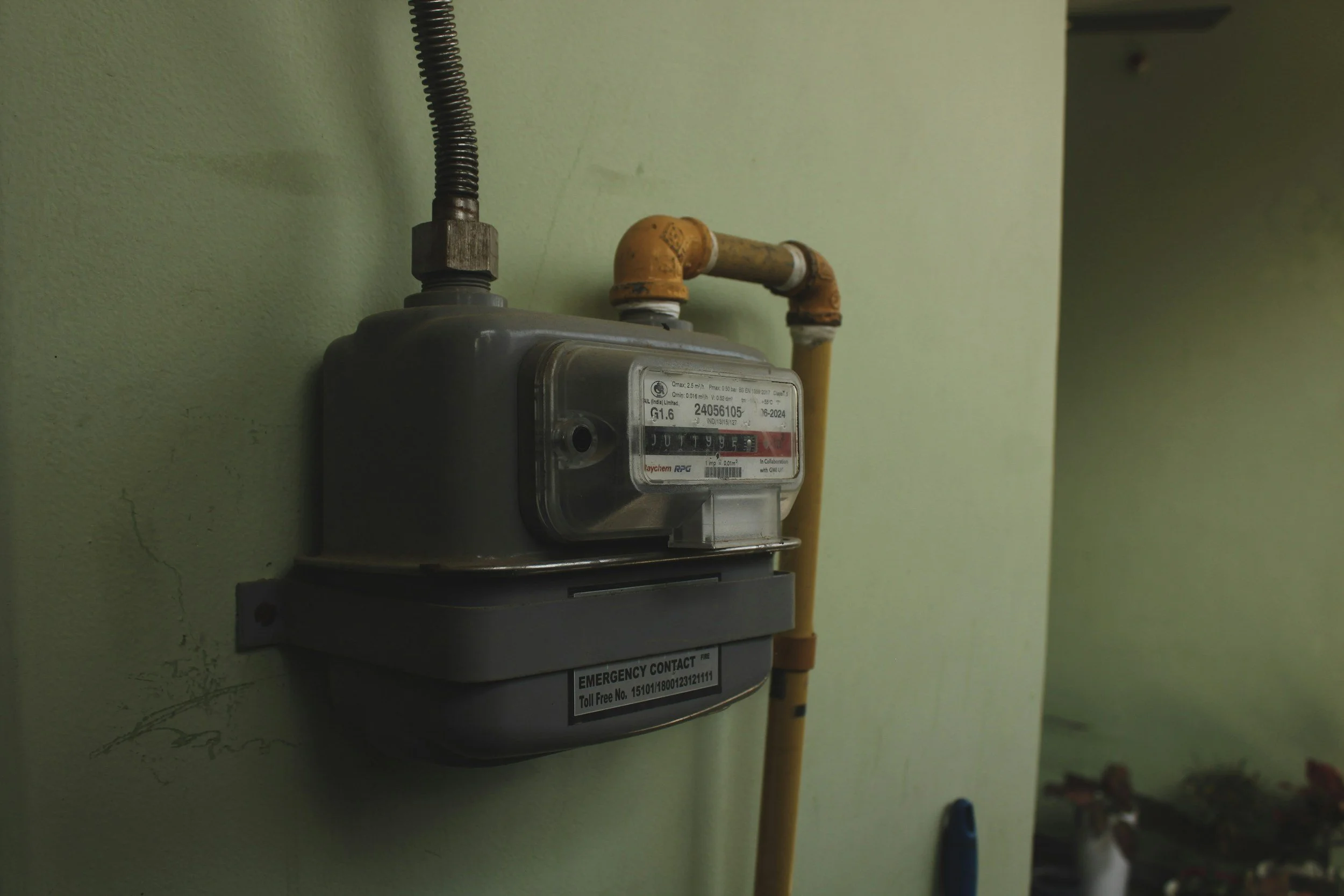 Electric utility meter attached to a pale green wall, with an orange pipe nearby.