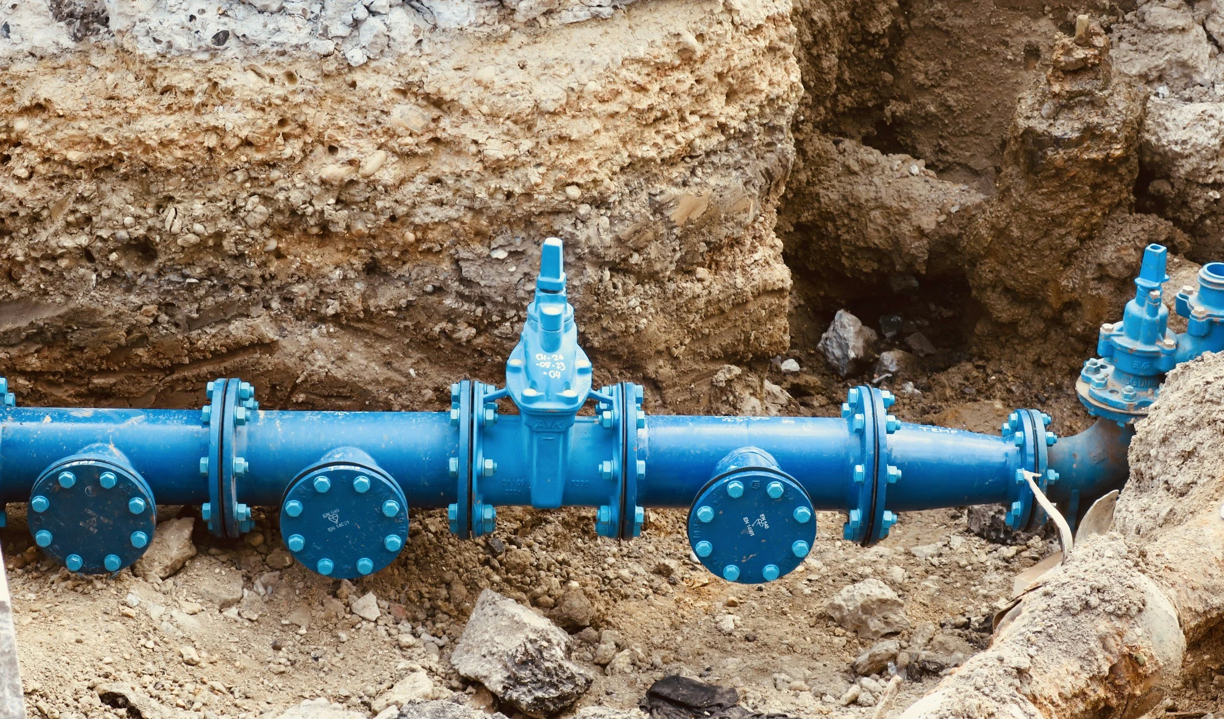 Blue underground water pipeline with valves in an excavation site with dirt and soil around.