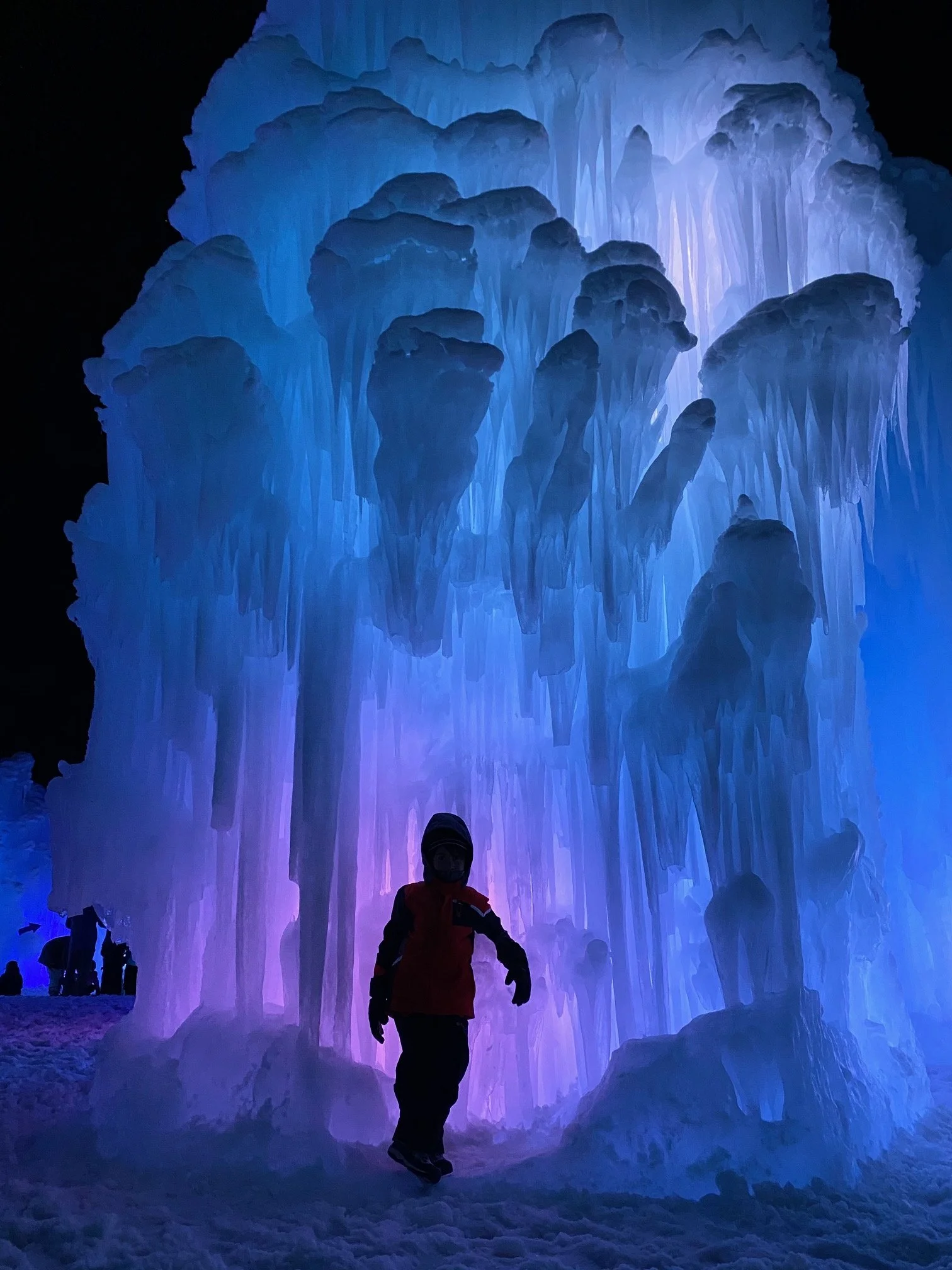 Person walking beside a towering illuminated ice formation