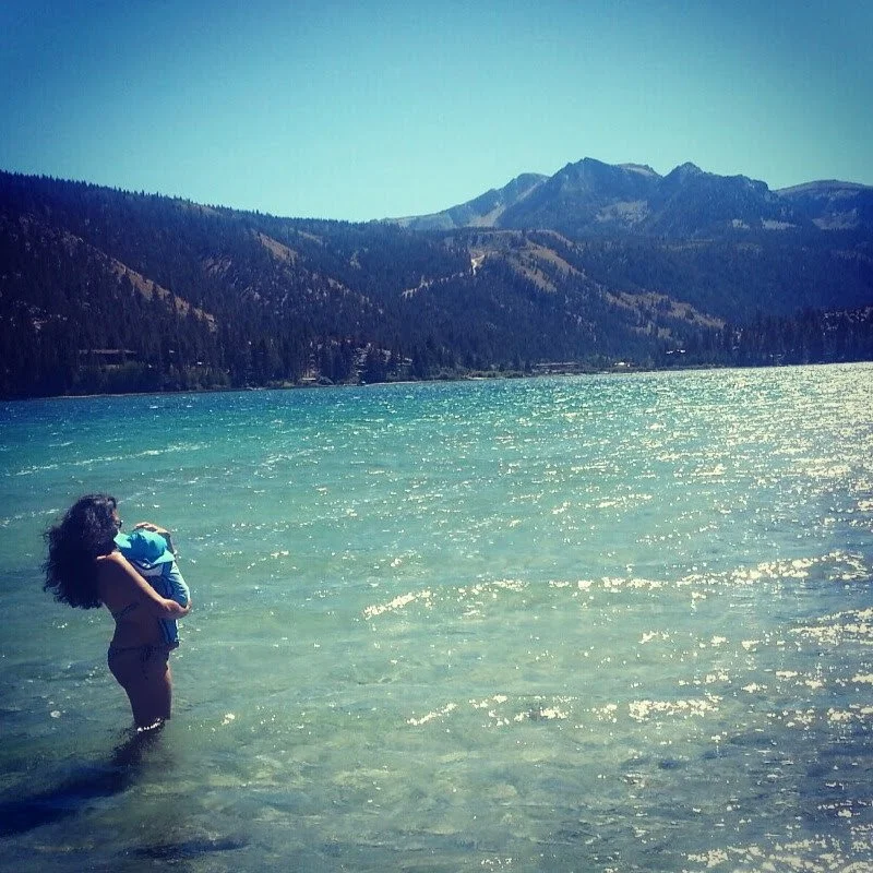 Mother holding a child in a mountain lake, evoking connection, safety, and healing