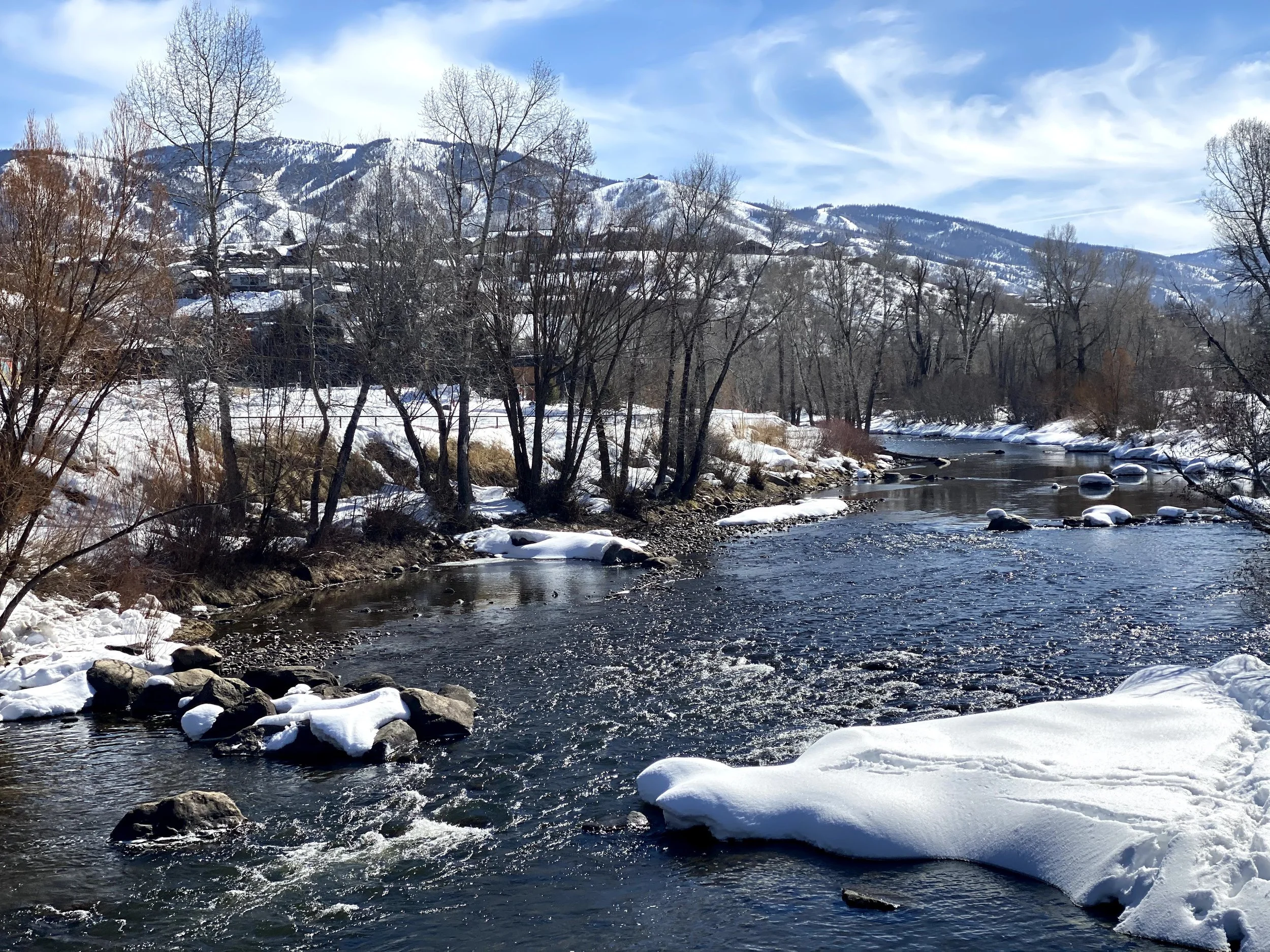 Snow-covered river flowing through a mountain valley beneath a blue winter sky.