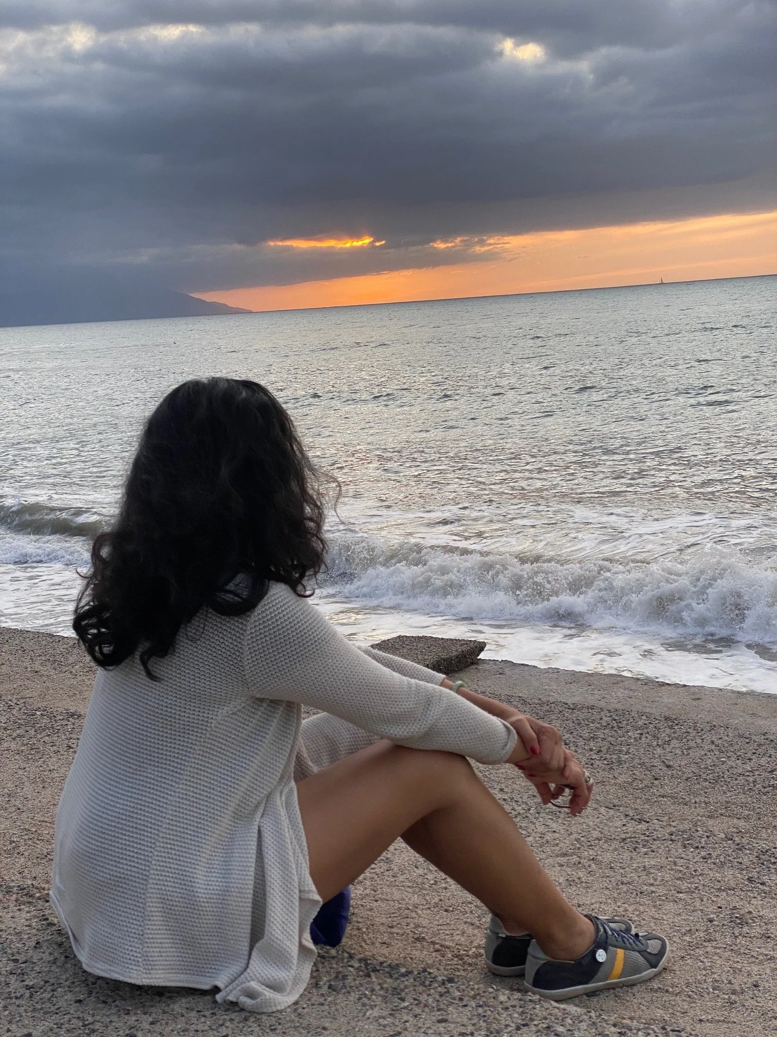 Woman sitting by the ocean at sunset, reflecting on her inner world.