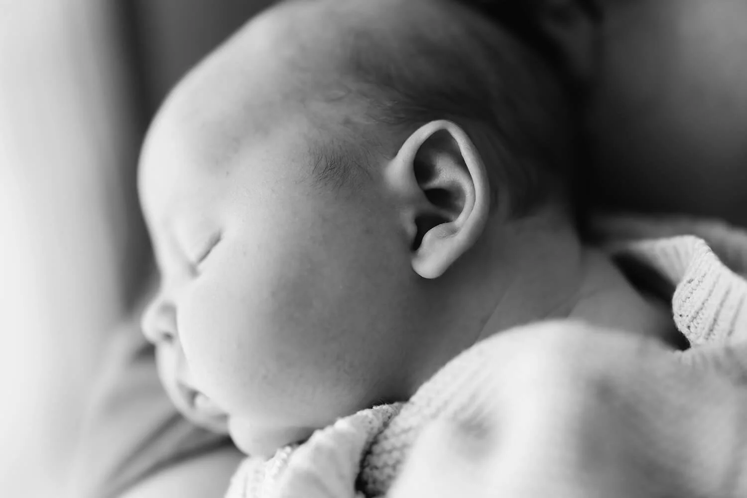 Close-up black and white photo of a sleeping baby resting on an adult's chest.