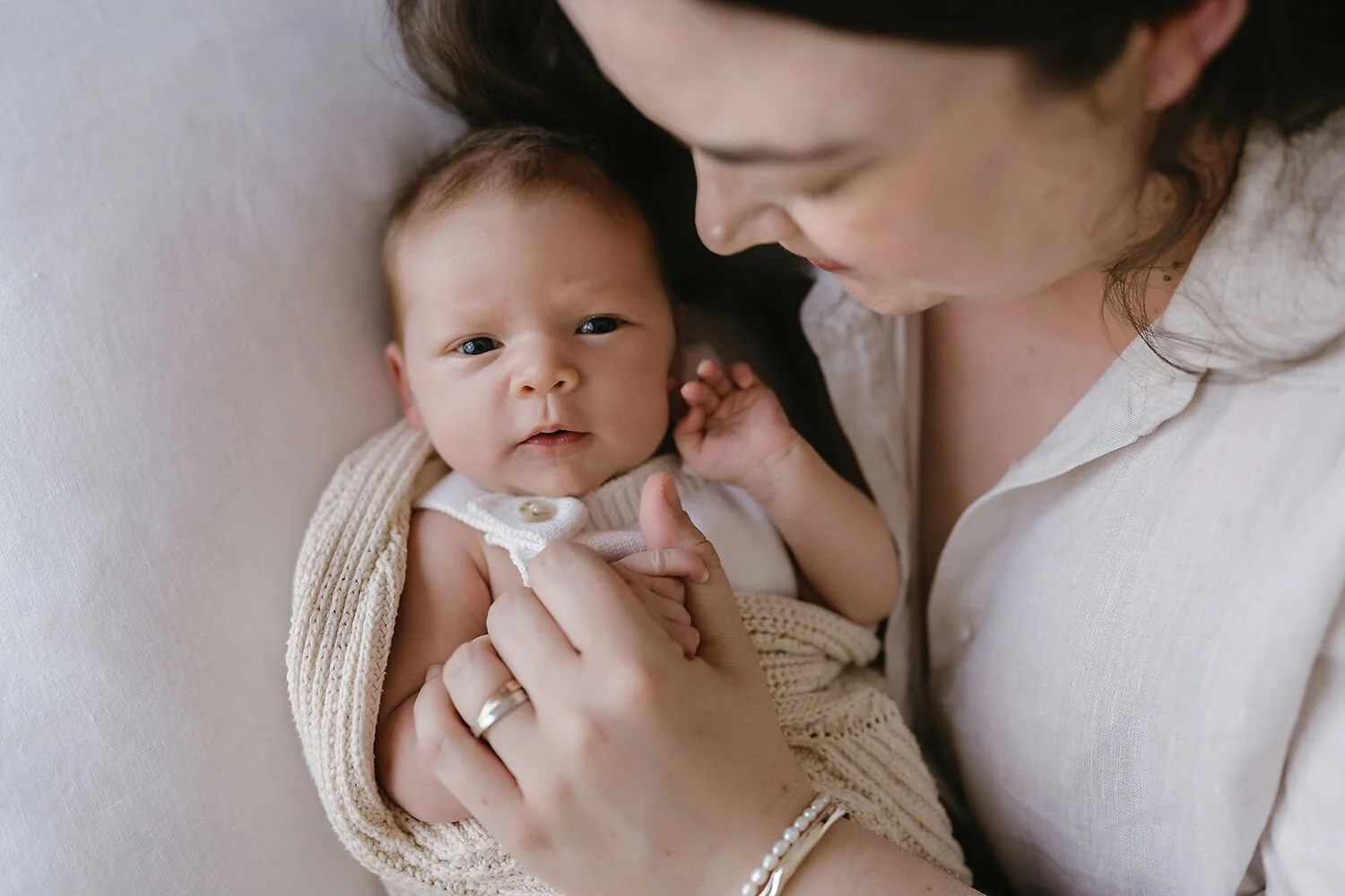 Photo of newborn baby with mother lying on bed looking up at Hobart newborn photographer