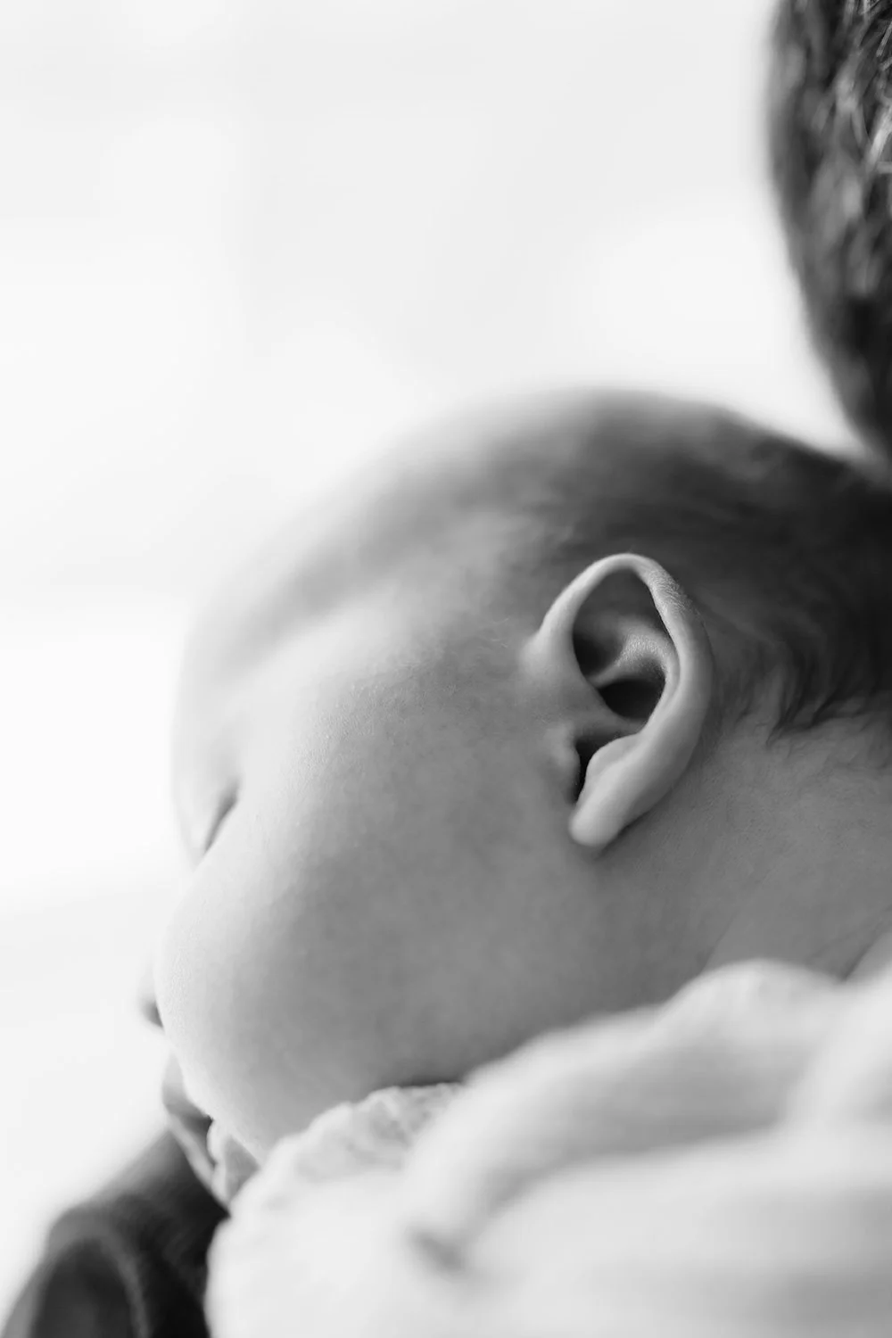 Close-up of a sleeping baby's face showing the nose, closed eye, and ear in black and white.