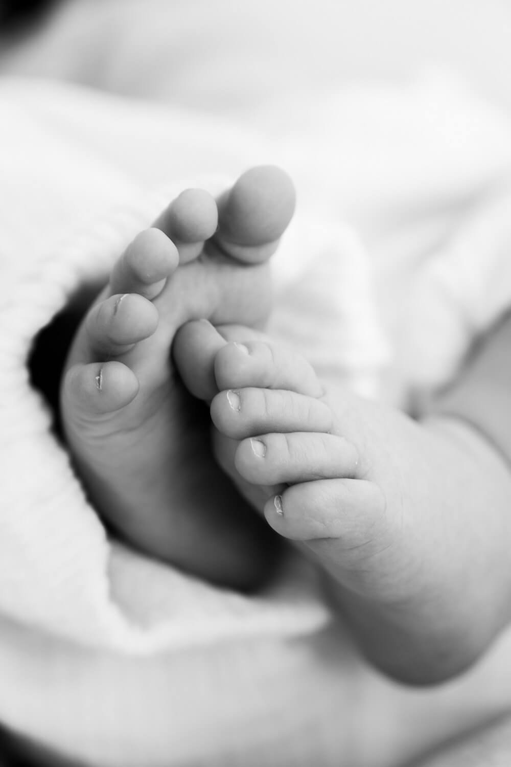 Close-up of a baby's tiny hand gripping an adult's finger in black and white.