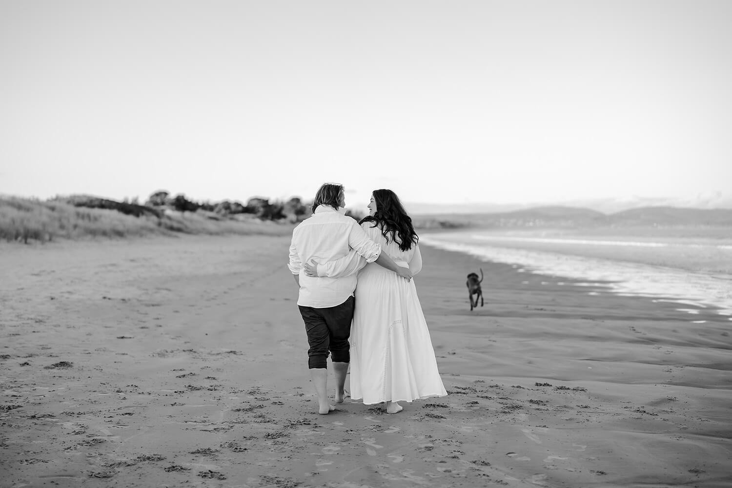 A couple walking on the beach with their dog, black and white photo.