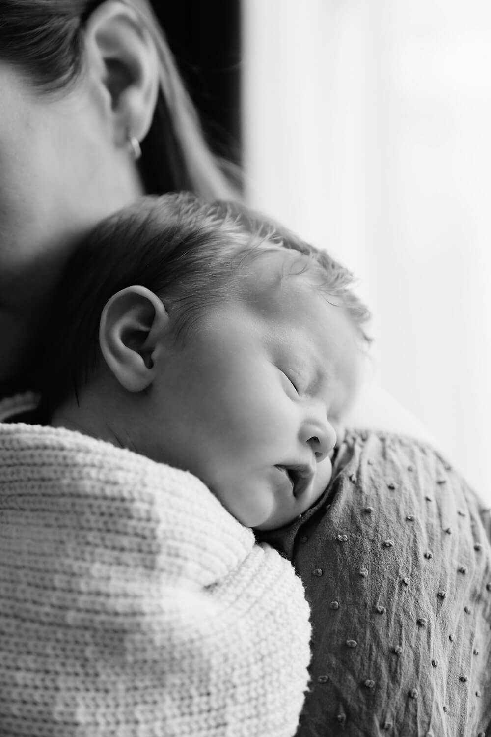 Black and white photo of a woman holding a sleeping fetus, close-up of her face and shoulder.