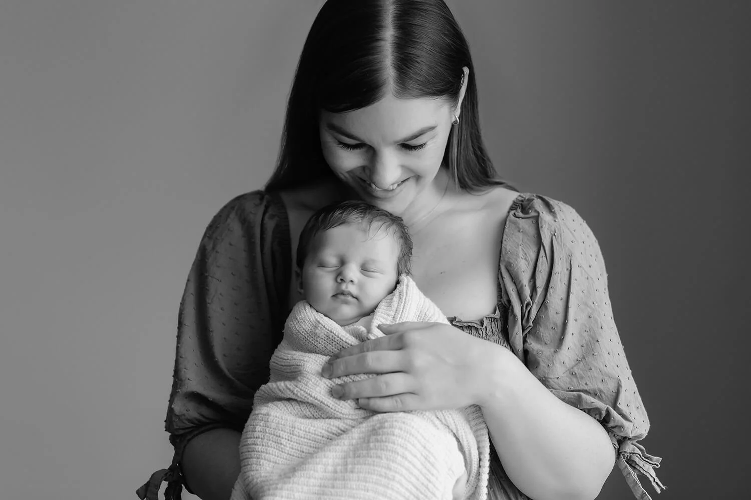Black and white photo of a mother holding her newborn baby close to her chest, both with peaceful expressions.