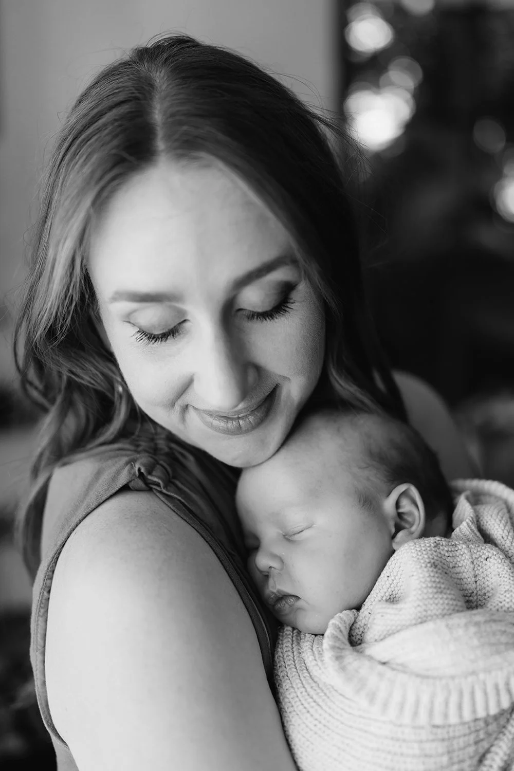 A woman holding a sleeping baby close to her chest, with her eyes closed and a gentle smile, in black and white.