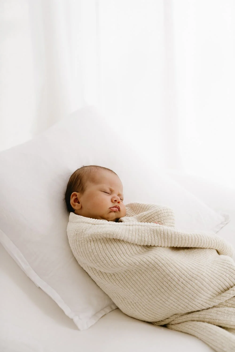 Newborn baby laying on pillow wrapped in a blanket being photographed by newborn photographer in Hobart