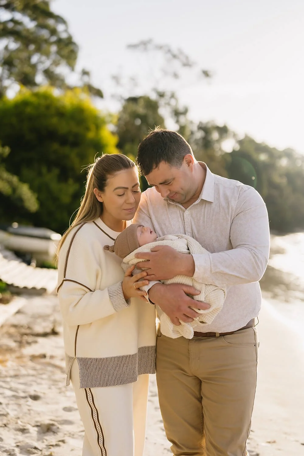 Couple on Hobart beach holding newborn baby being photographed by family photographer