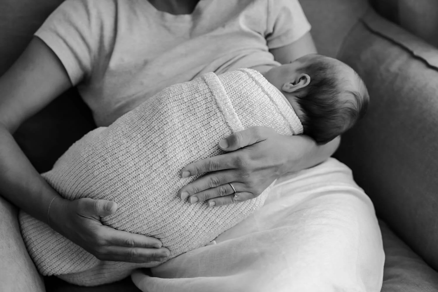 A person gently holding a newborn baby wrapped in a textured blanket, resting on their lap.