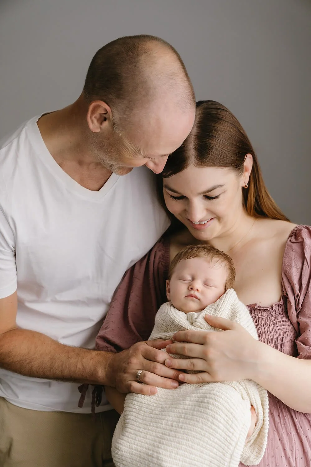 Couple holding their newborn baby in their arms and being photographed by newborn photographer in Hobart