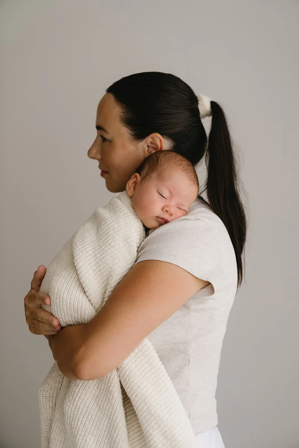 A woman holding a sleeping baby close to her chest.
