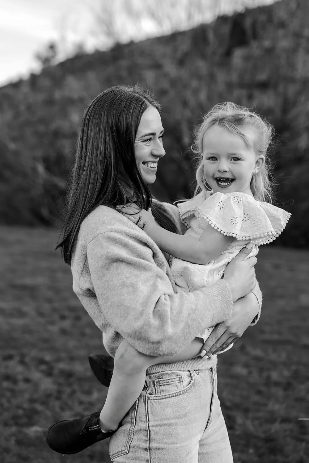A woman holding a young girl in an outdoor setting, both smiling and appearing happy.