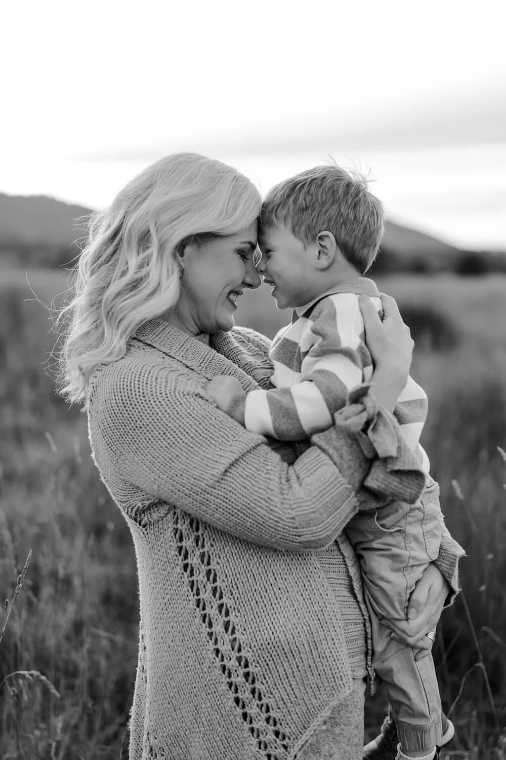 A woman and a young boy smiling and touching foreheads while holding each other in an outdoor field.