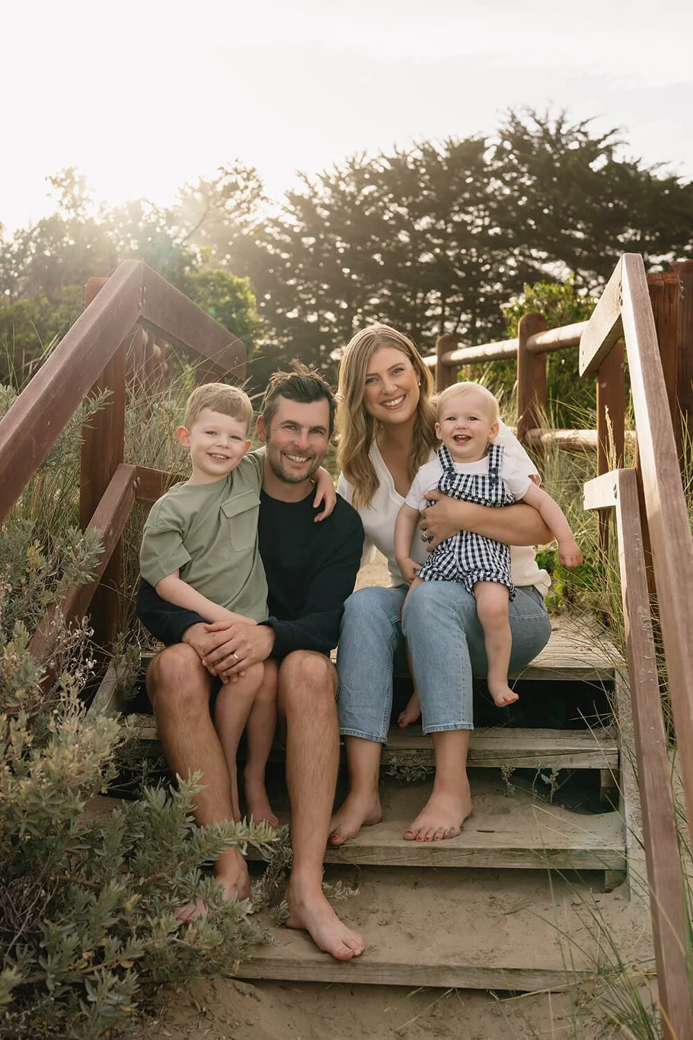 A family of four sitting on a wooden step at Roches Beach Hobart at sunset, smiling at the camera.