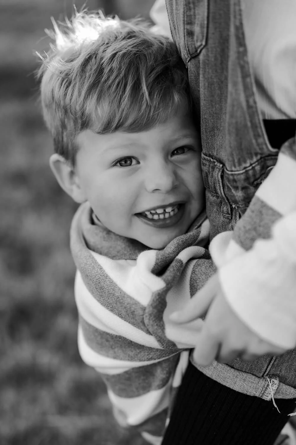 A young child with curly hair smiling and hugging an adult, visible only partially, in a close-up black-and-white photo.