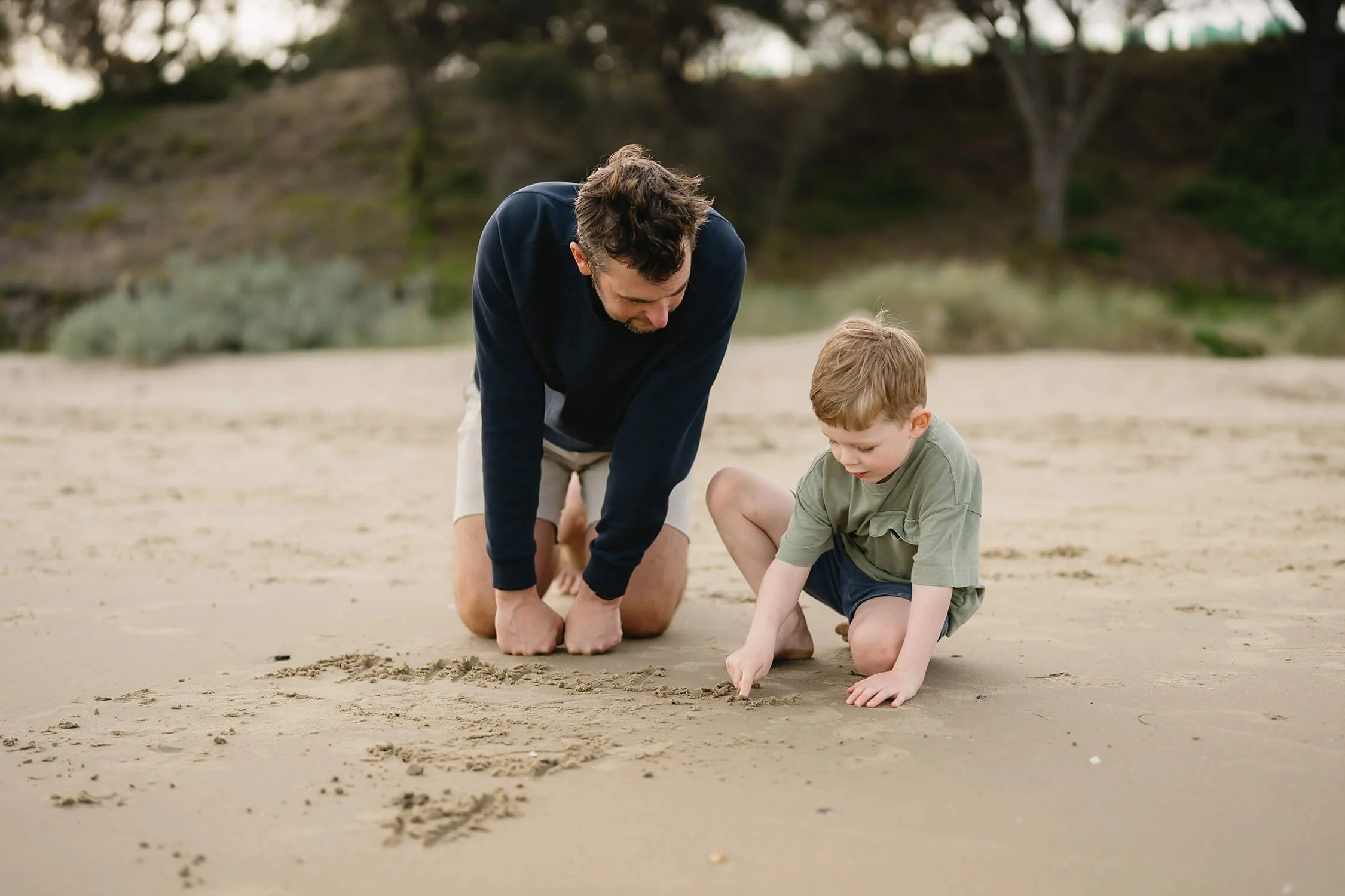 A man and a young boy drawing in the sand on a beach.