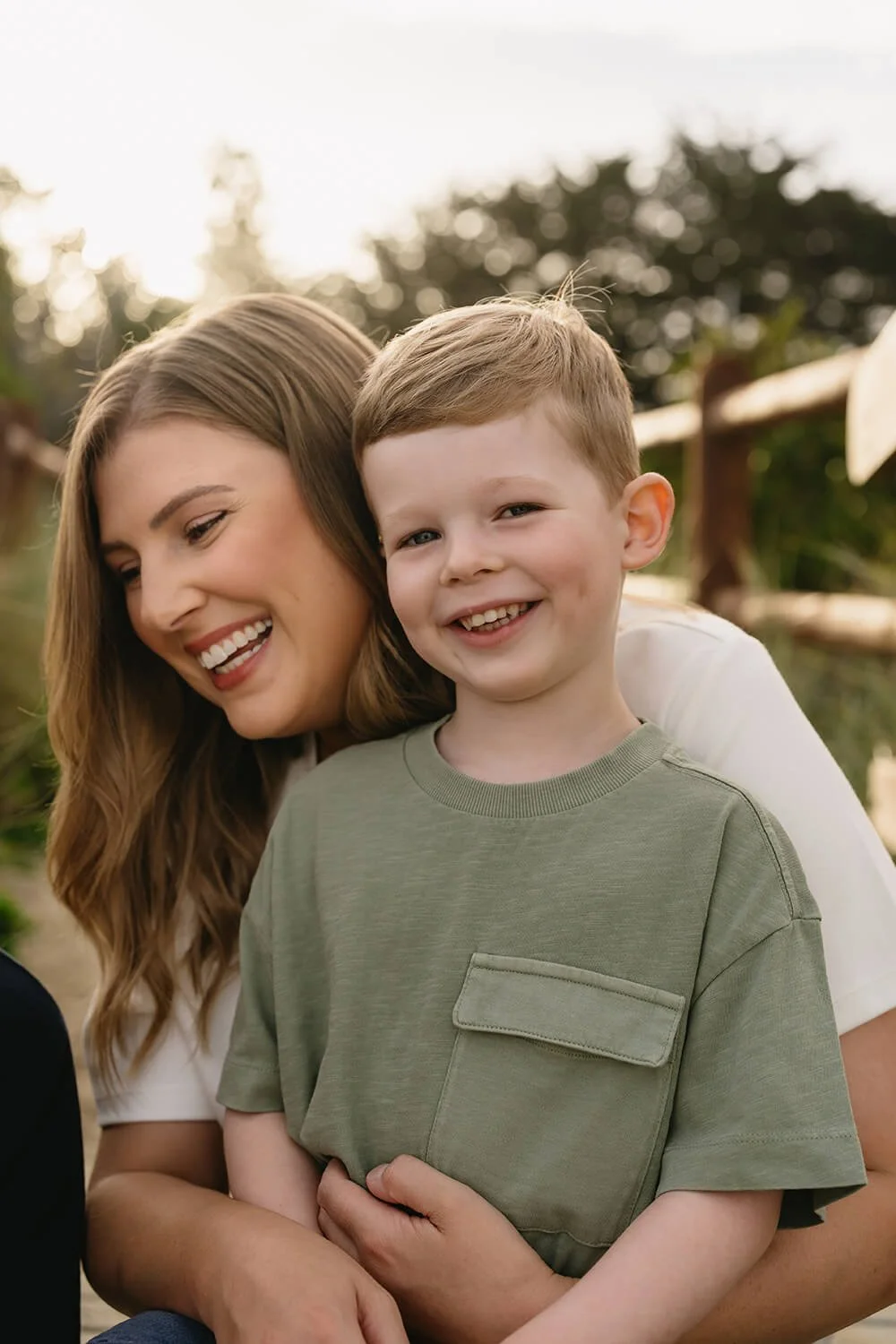A smiling woman and young boy outdoors enjoying a sunny day.