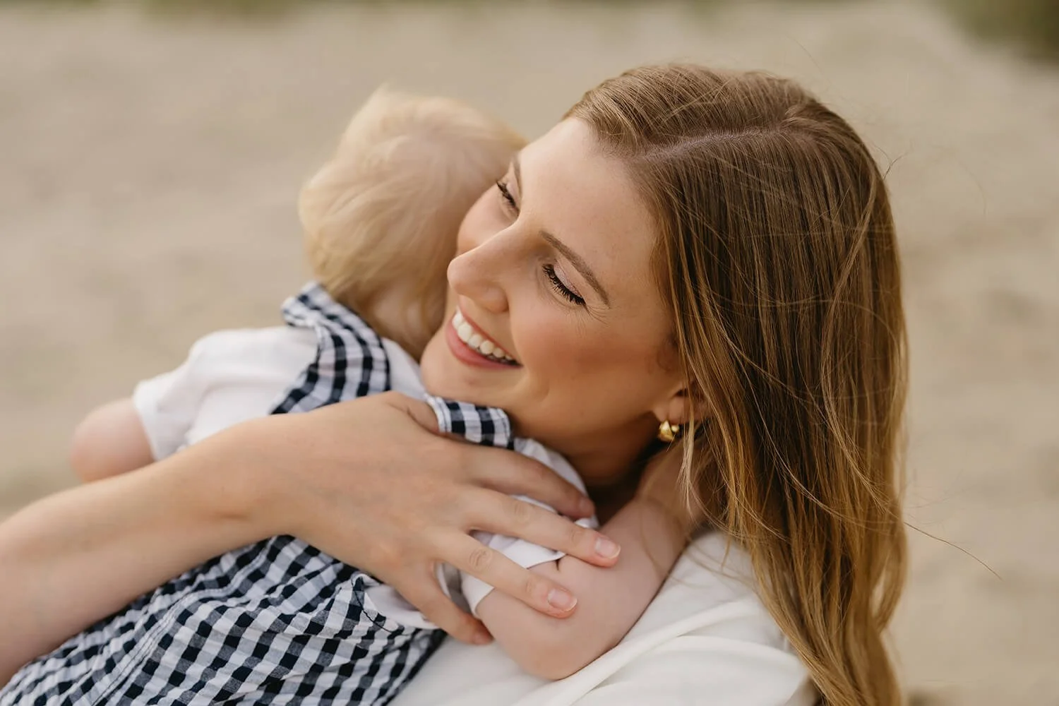 A woman with blonde hair is hugging a young boy with blonde hair, both smiling warmly.