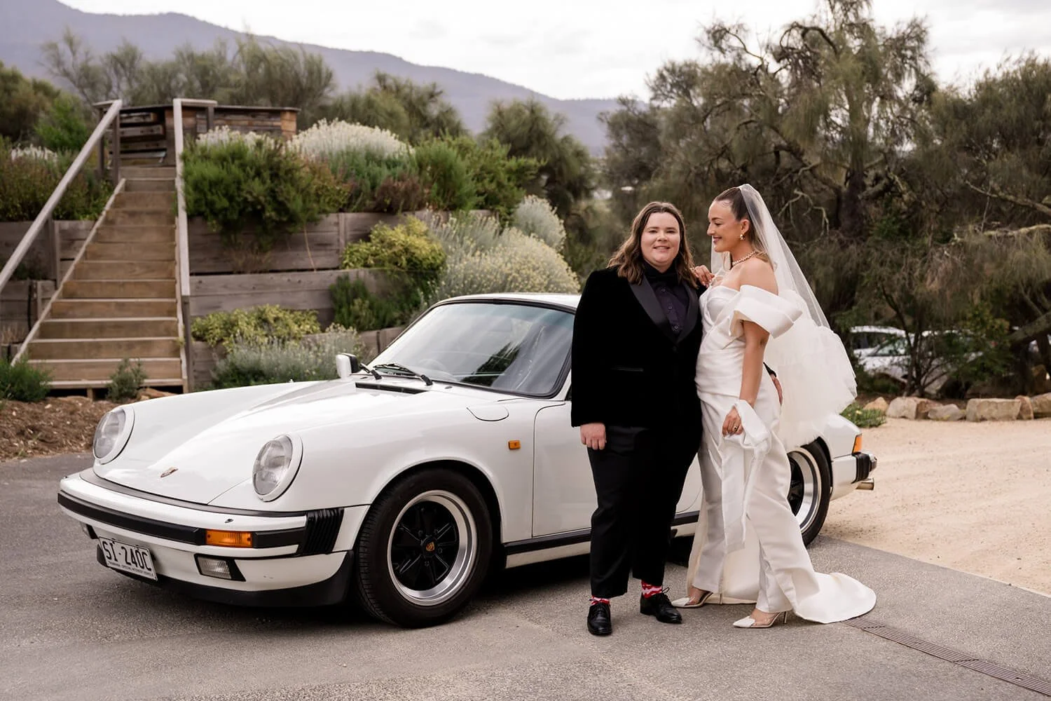 Same sex couple standing in front of a vintage car being photographed on their wedding day